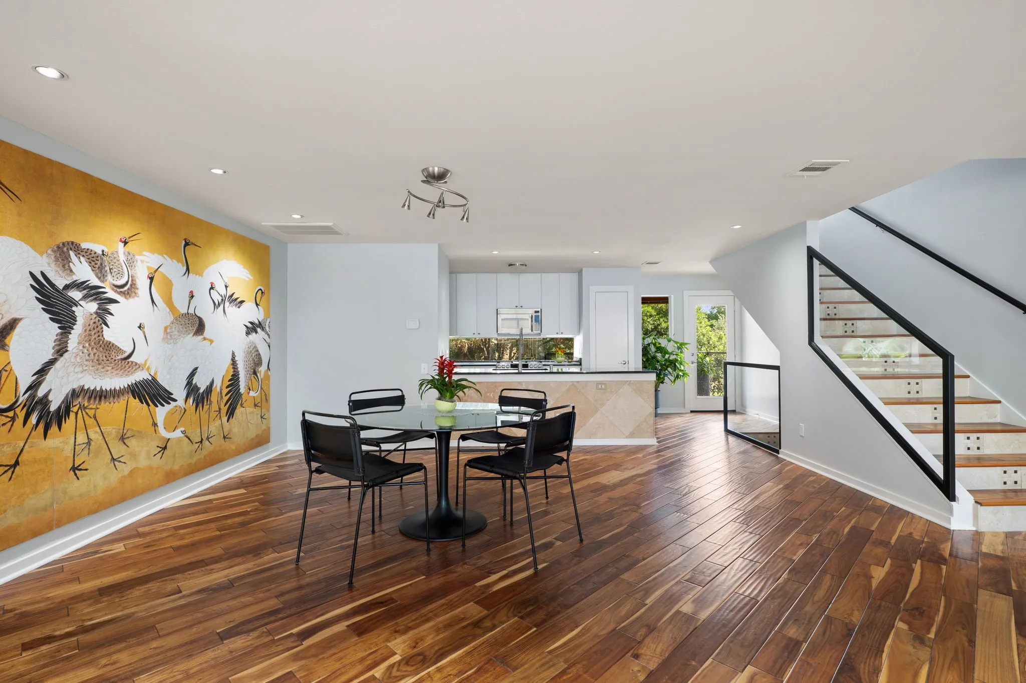 Open-concept living area with rich wood-finish flooring, recessed lighting, and a modern staircase featuring black metal railings