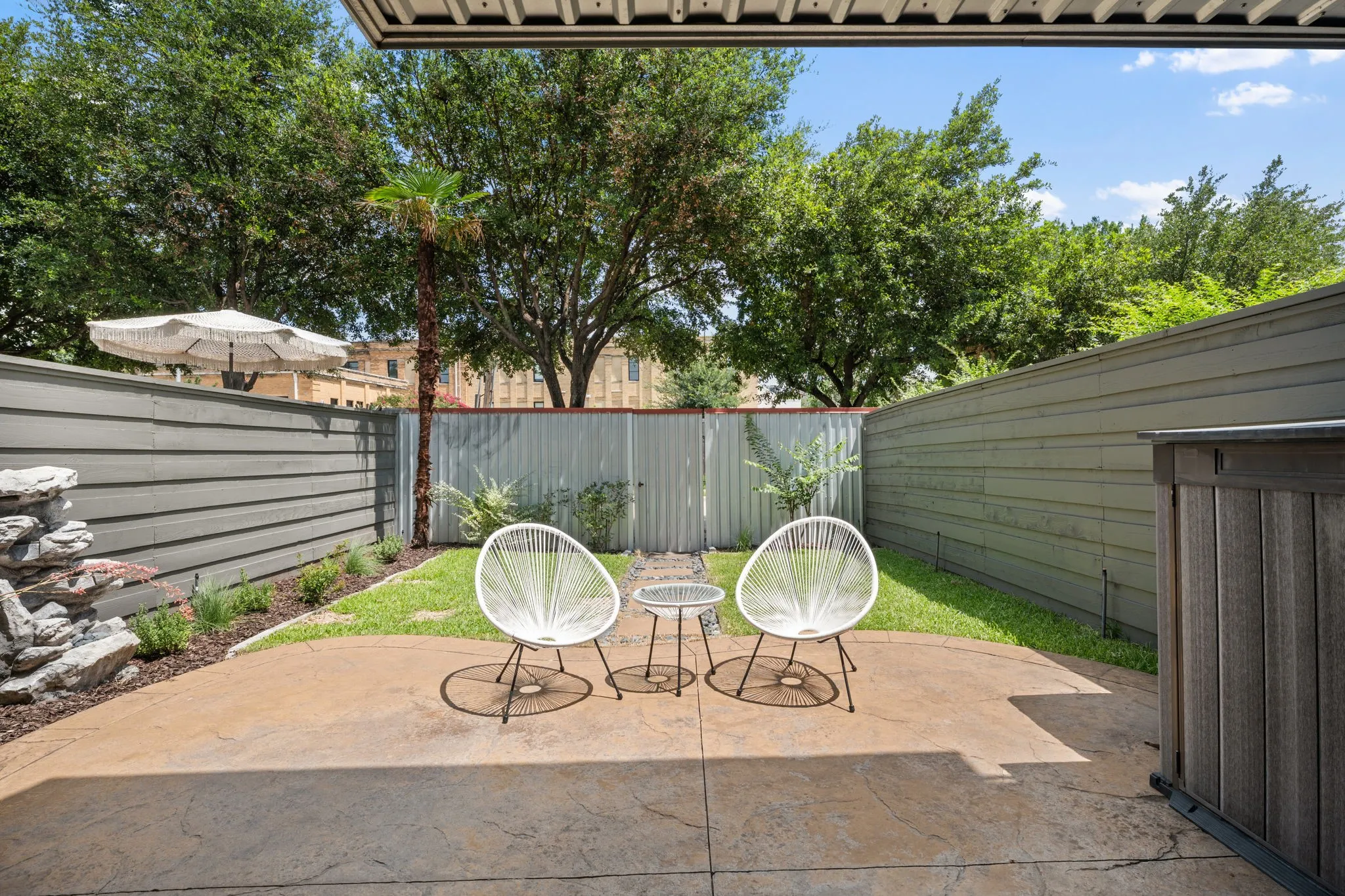 Private outdoor patio featuring a stamped concrete surface, manicured lawn, and a stacked stone water feature