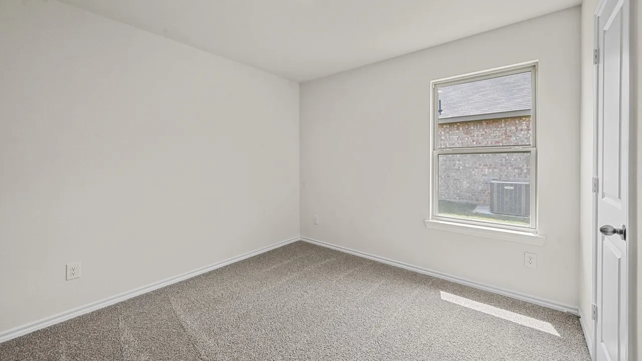 Carpeted interior room with a window providing natural light and an exterior view of brick construction