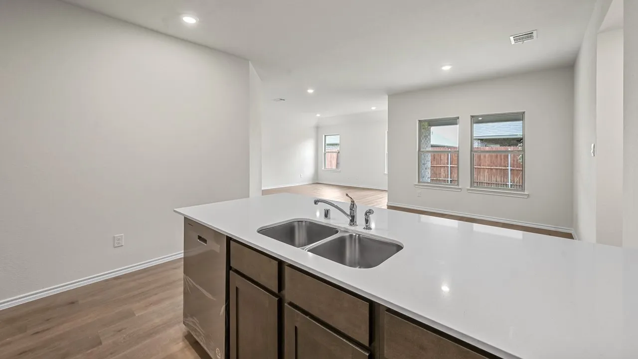 Kitchen island featuring a double basin stainless steel sink, a chrome faucet, light-colored countertop, and dark wood cabinetry