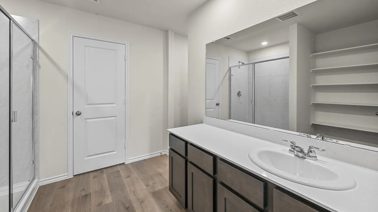 Double vanity with a white countertop and integrated sink, chrome fixtures, built-in shelving, glass-enclosed shower, and wood-finish flooring