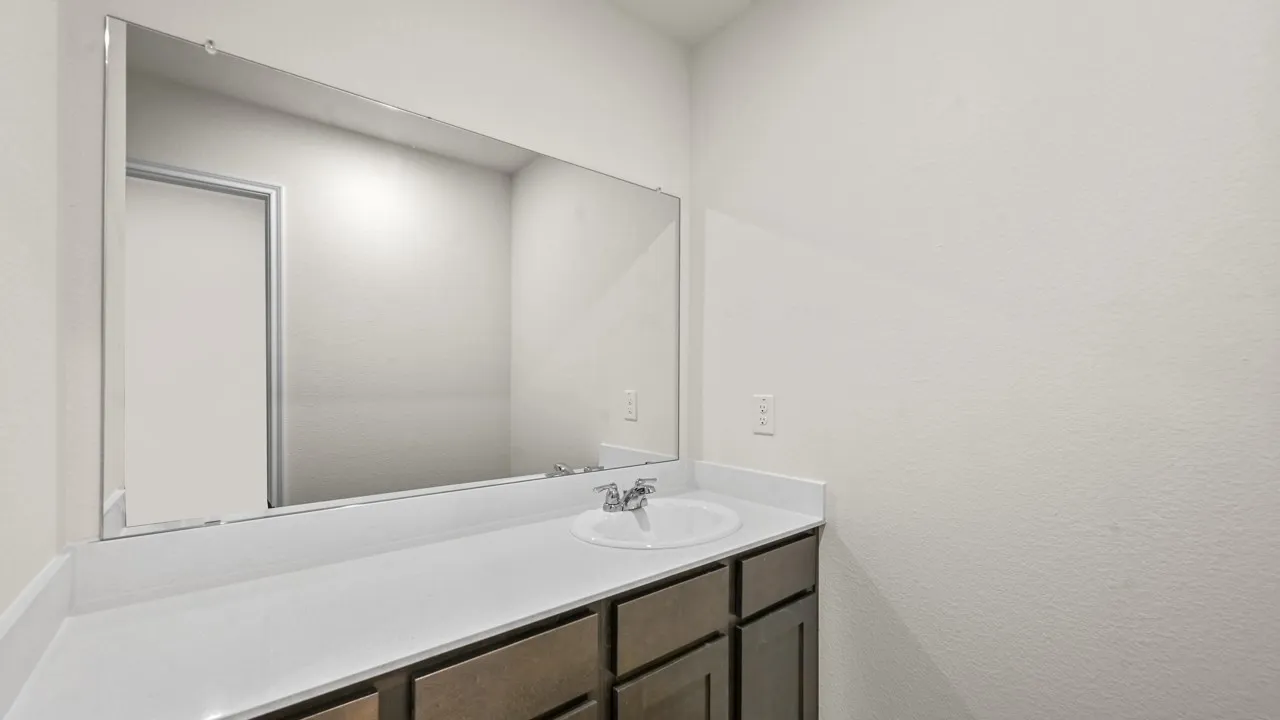Spacious bathroom vanity featuring an integrated sink, polished chrome faucet, expansive wall-mounted mirror, and wood-finish cabinetry