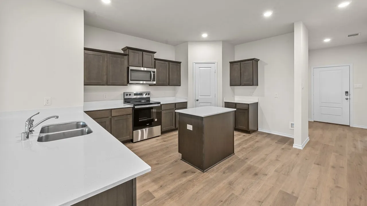 Spacious kitchen featuring an island, wood-finish flooring, white countertops, dark cabinetry, and stainless steel appliances