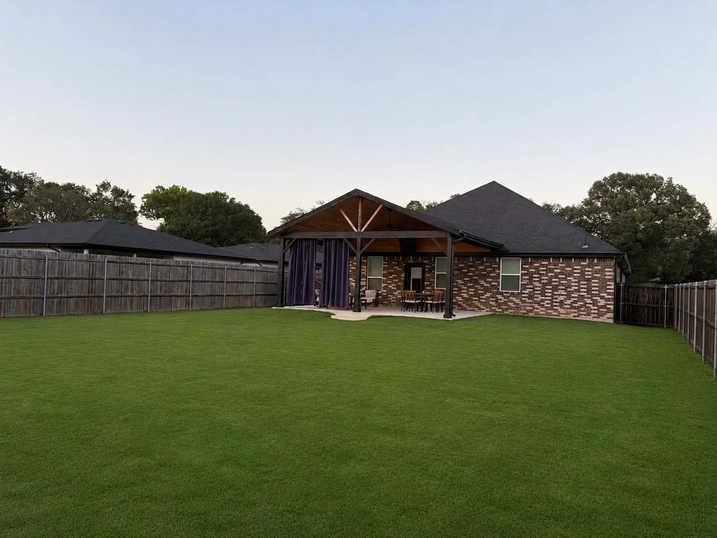 Expansive backyard featuring a manicured lawn, full privacy fencing, and a covered patio with exposed wood beams