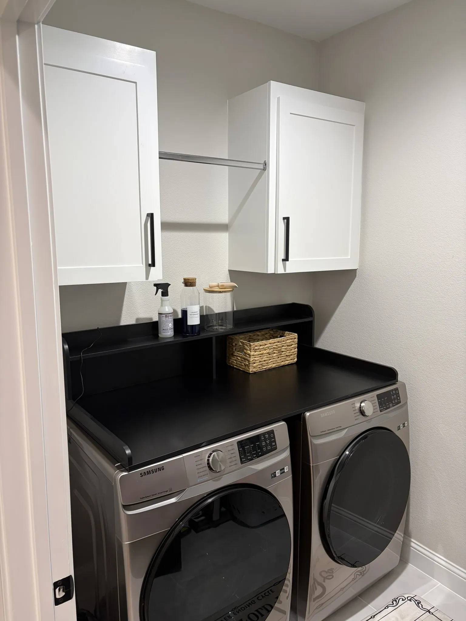 Laundry area featuring white shaker-style cabinetry with matte black hardware, a black countertop, and an integrated drying rod