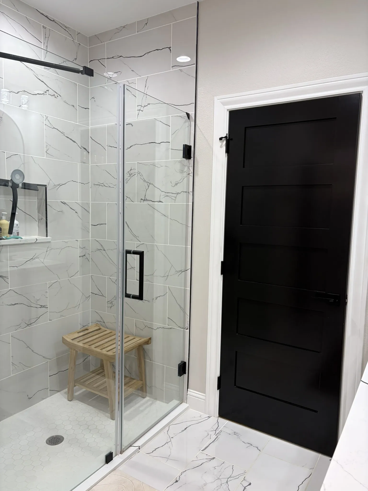 Modern bathroom featuring a frameless glass shower enclosure with matte black hardware, white subway tile with dark veining, and a black paneled door with matte black hardware