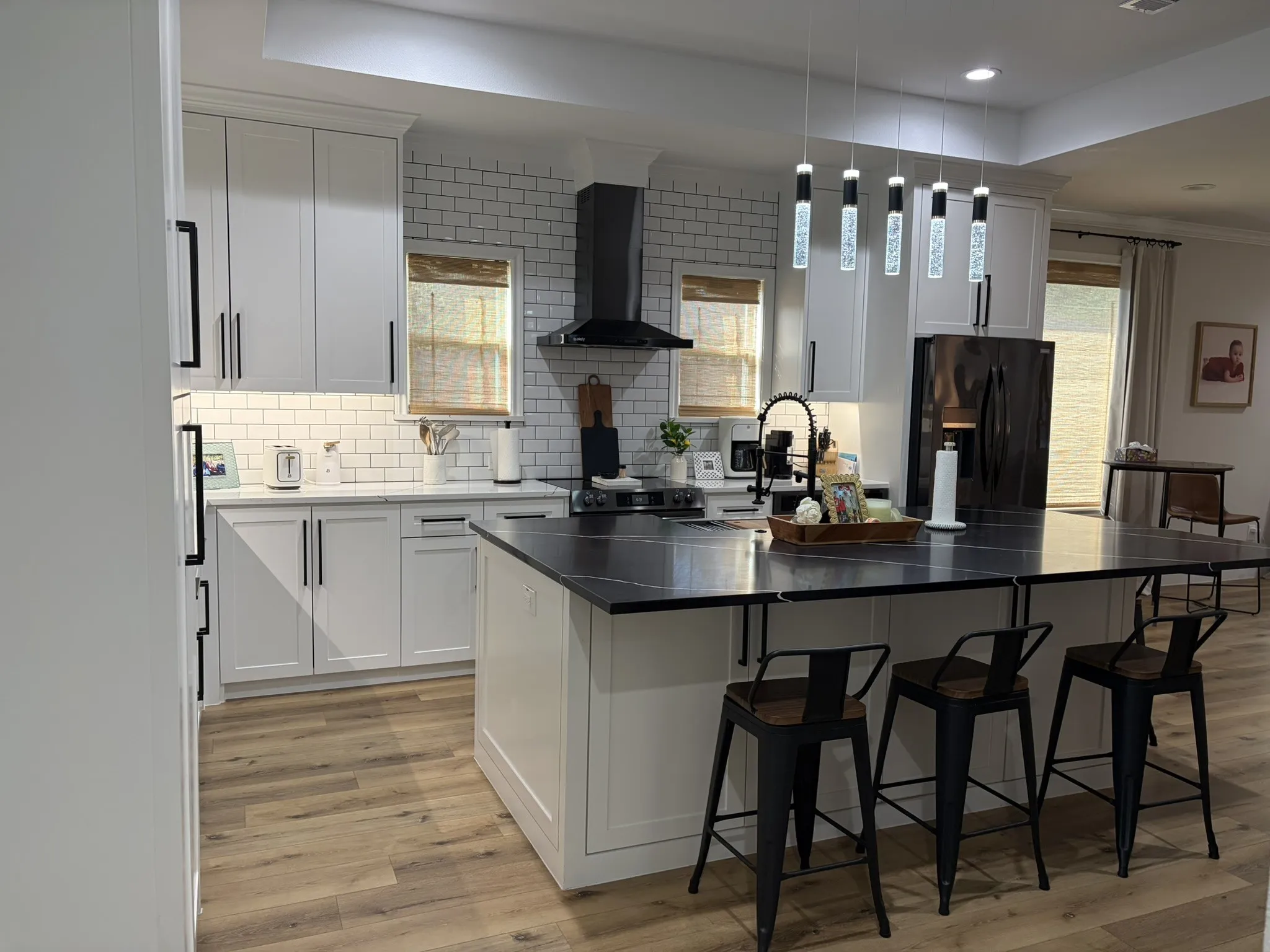 Kitchen featuring a central island with countertop seating, white shaker cabinetry, white subway tile backsplash, dark countertops, and wood-finish flooring