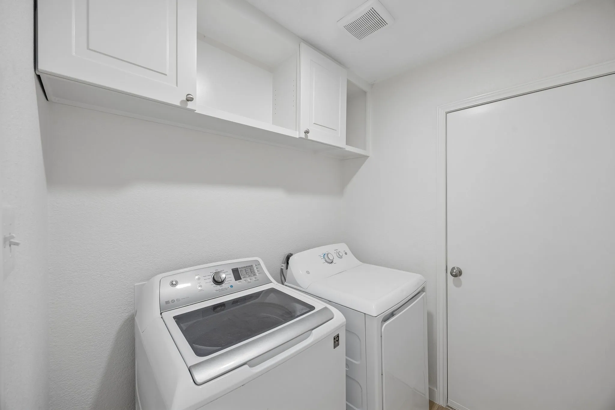 Convenient interior laundry room with upper storage cabinets and space for full-size washer and dryer.