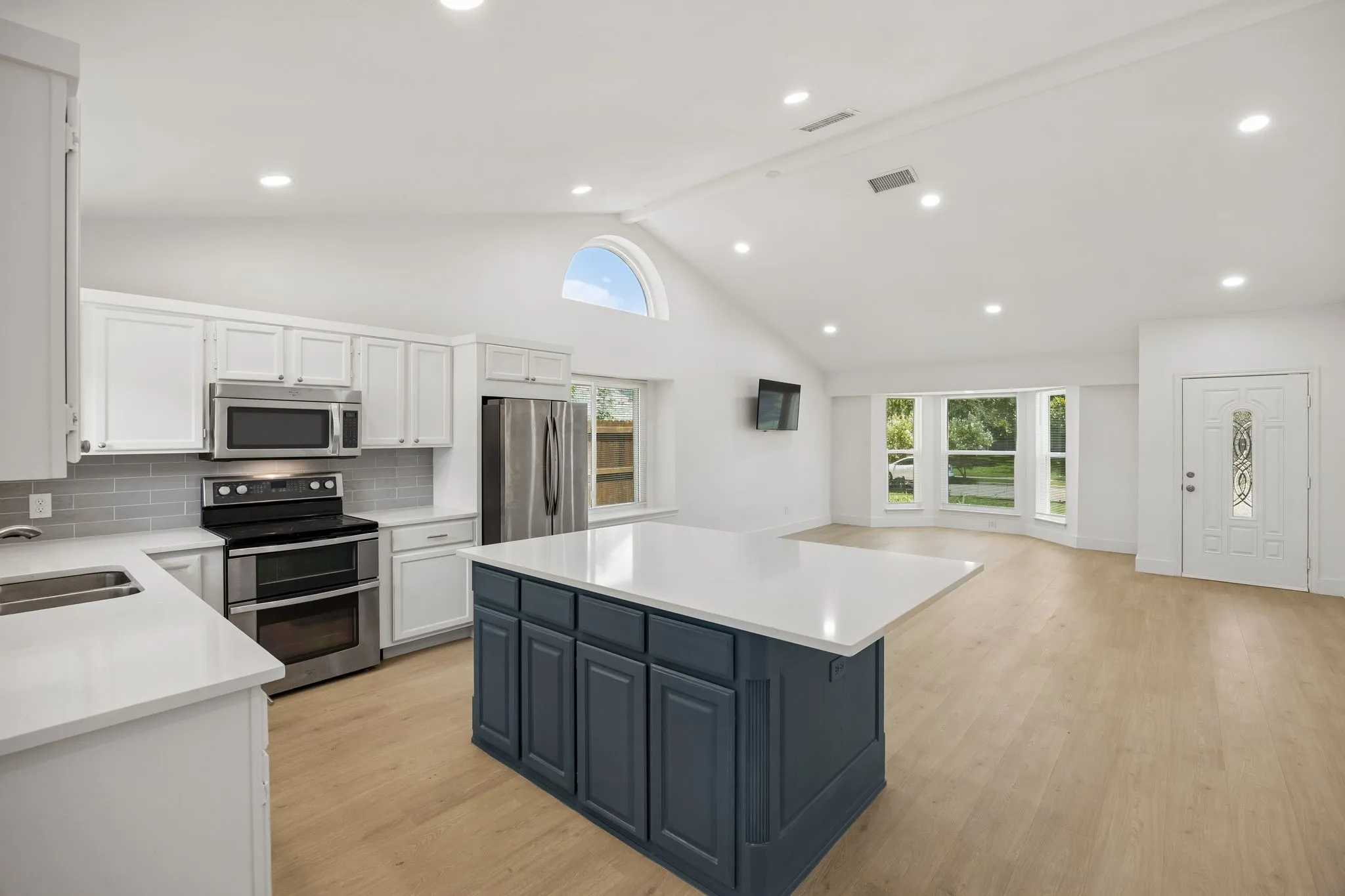 The open-concept design seamlessly connects the kitchen and living room, highlighted by soaring vaulted ceilings, abundant natural light, and a spacious layout ideal for modern living.