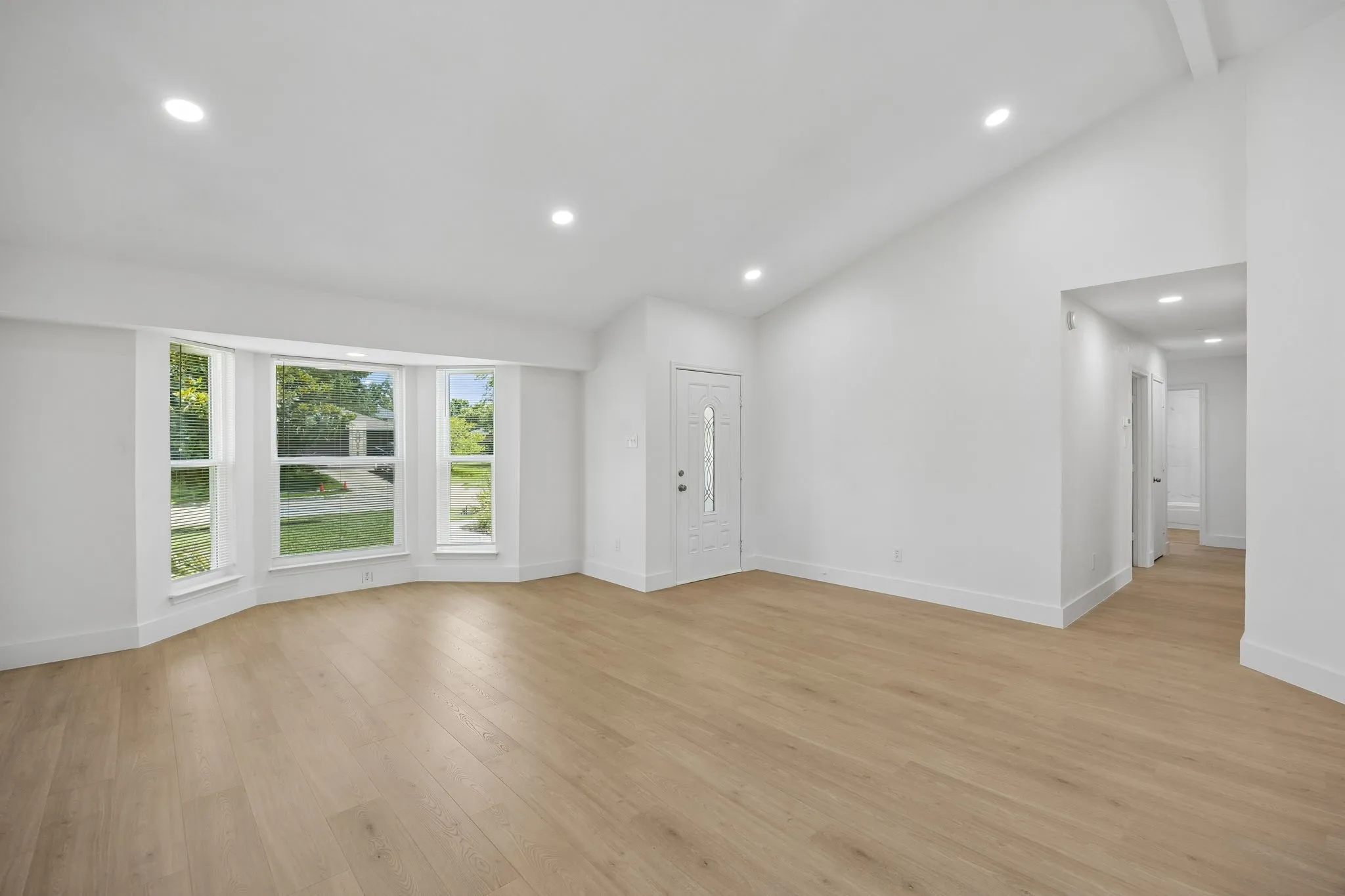 The expansive living room offers endless furniture arrangement possibilities, enhanced by vaulted ceilings, recessed lighting, and a wall of windows that fills the space with natural light.