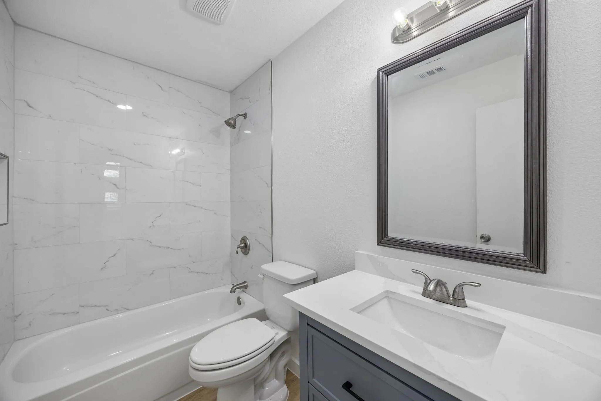 Beautifully renovated full bathroom featuring quartz countertops, designer tile surround, updated vanity, and modern fixtures.