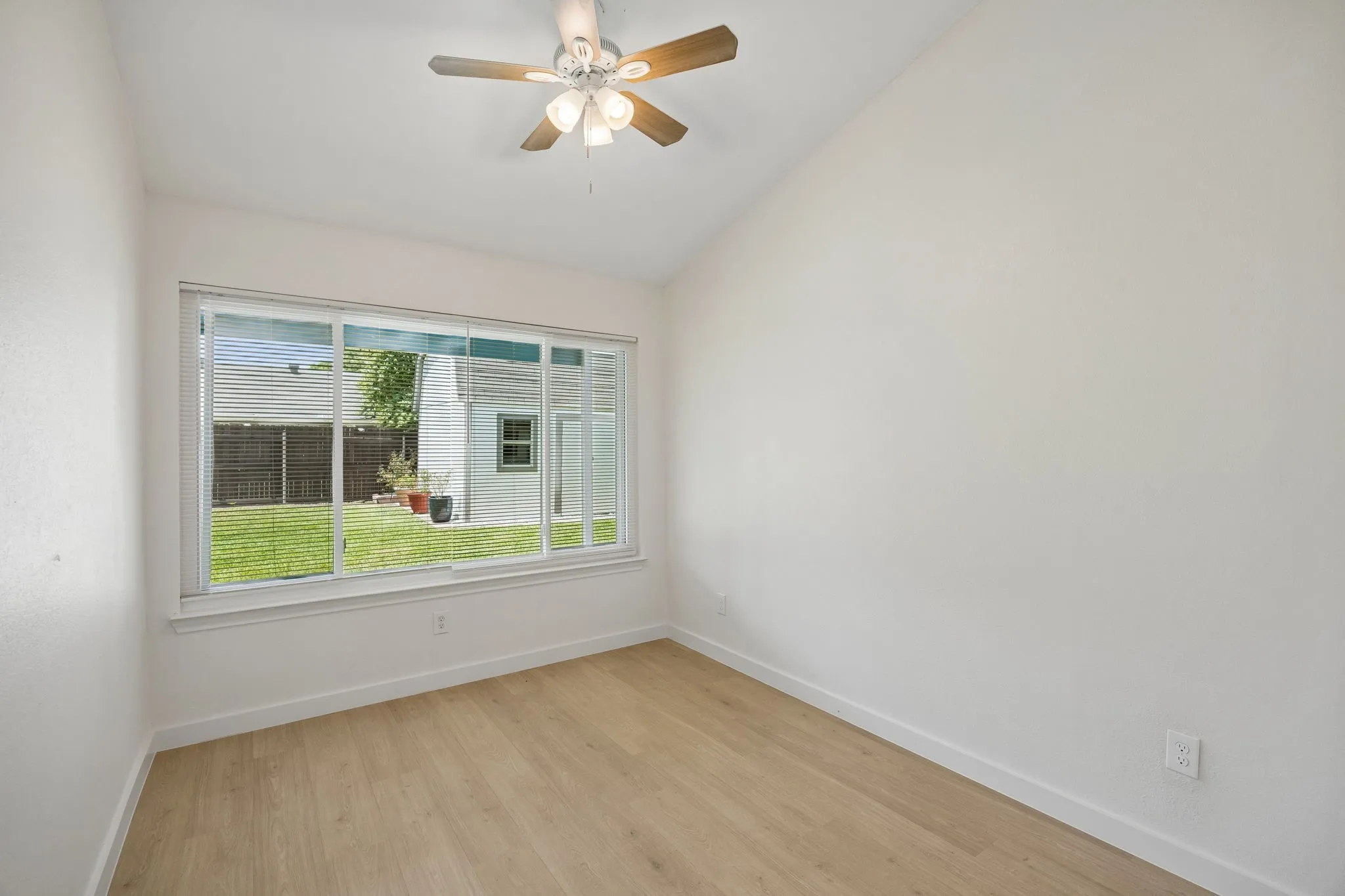 Spacious bedroom overlooking the backyard with vaulted ceiling, ceiling fan, luxury flooring, and oversized picture window.