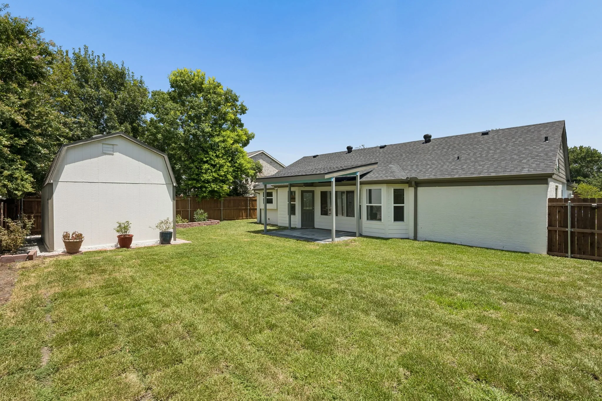 Backyard showcasing the large backyard, covered patio, mature trees, and detached storage shed.