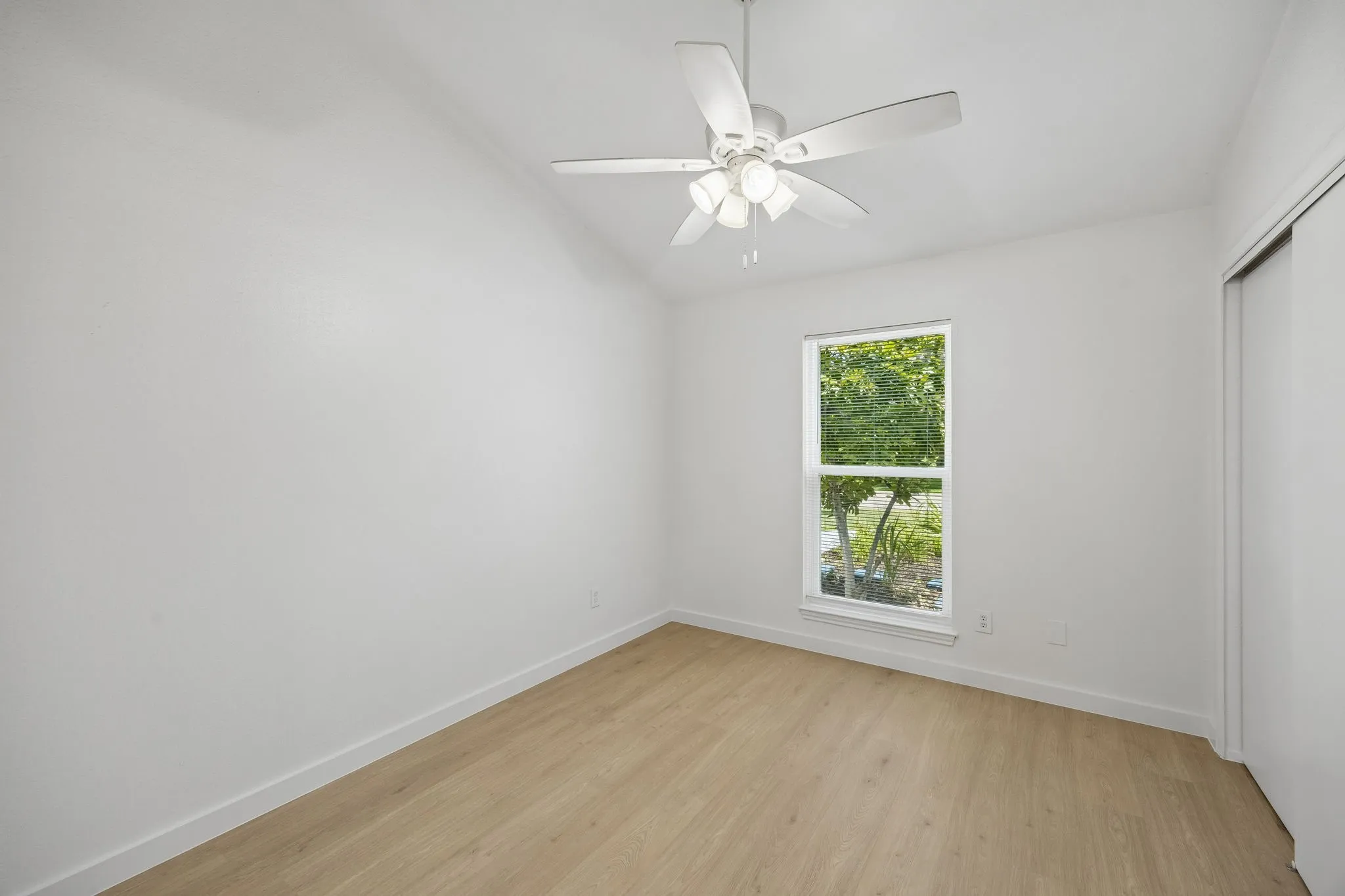 Bright secondary bedroom with vaulted ceiling, large front-facing window, neutral finishes, and generous closet space.