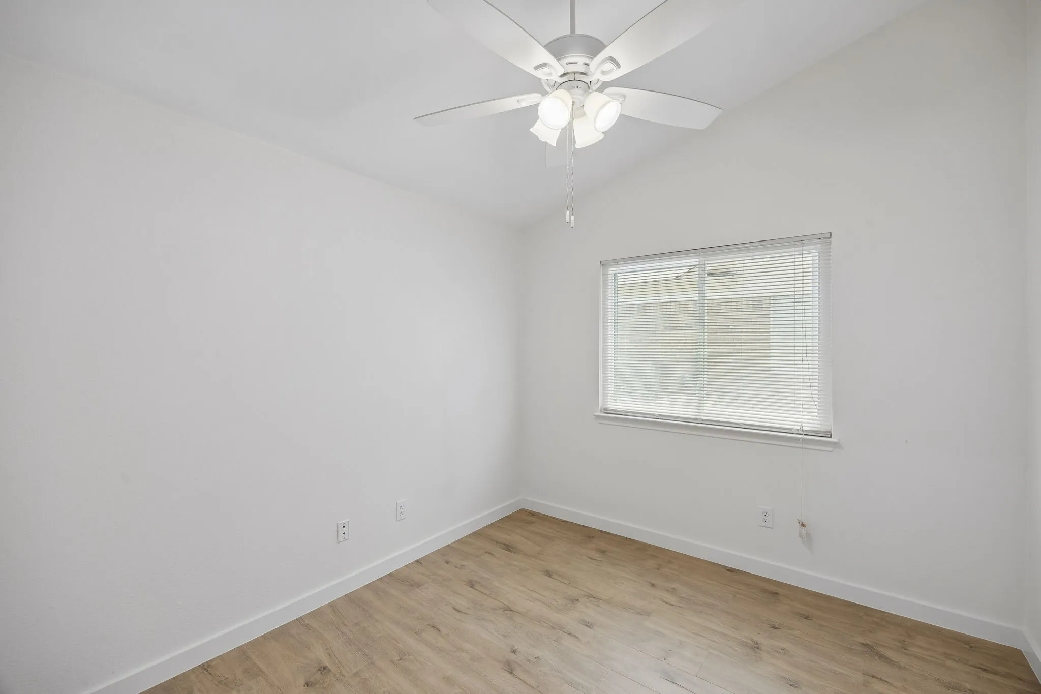 Secondary bedroom with vaulted ceilings, updated flooring, fresh neutral paint, ceiling fan, and abundant natural light.