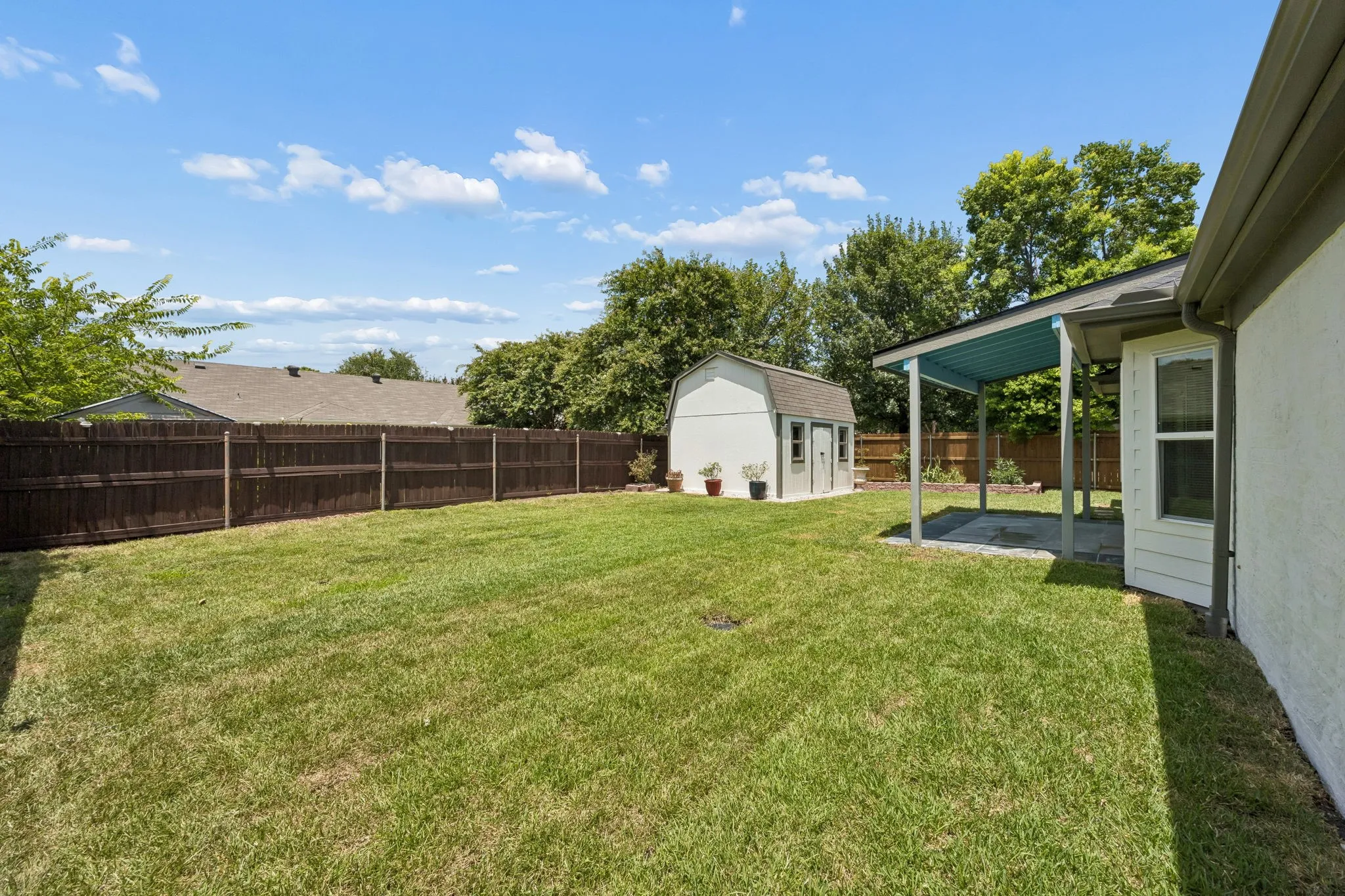 Expansive fenced backyard with lush lawn, storage building, and plenty of room for play, pets, or future outdoor living.