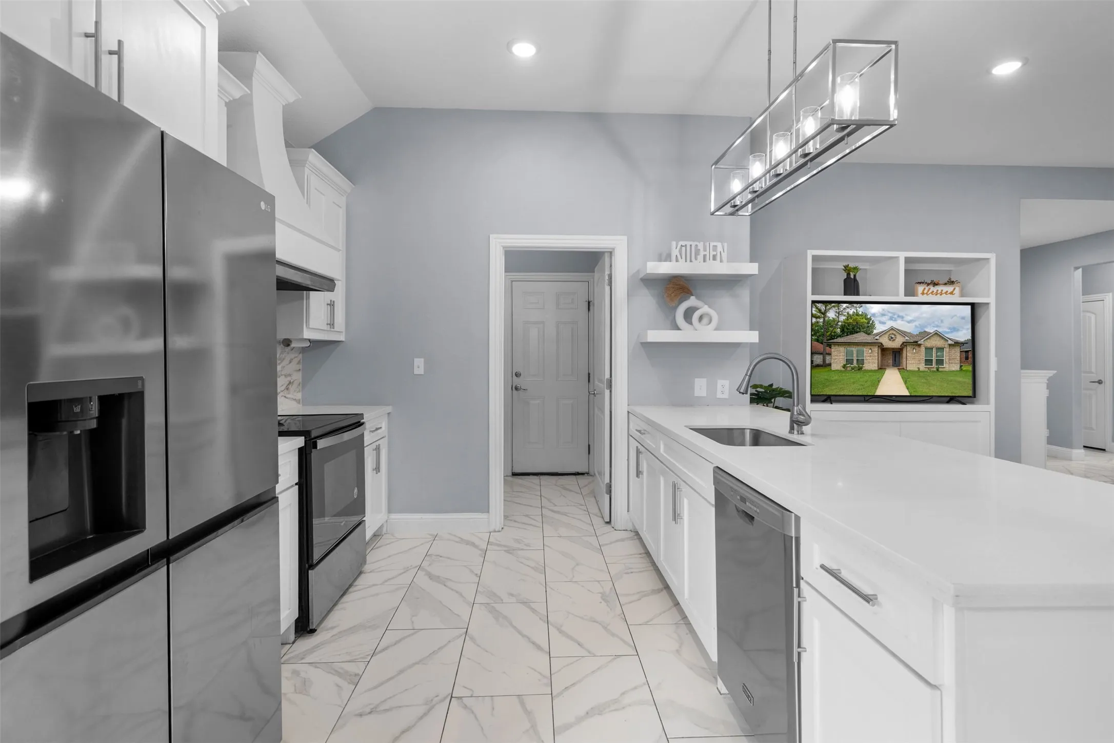 Kitchen featuring stainless steel appliances, white cabinets, light stone counters, hanging light fixtures, and light marble finish floors