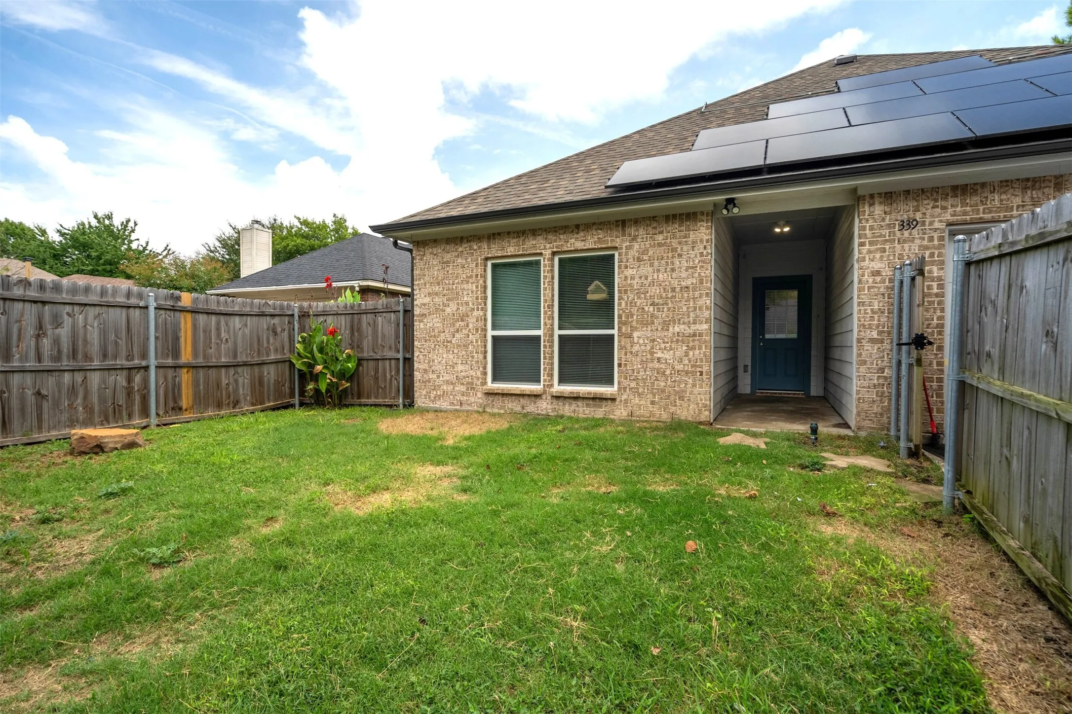 Back of property with a fenced backyard, brick siding, solar panels, a shingled roof, and a patio