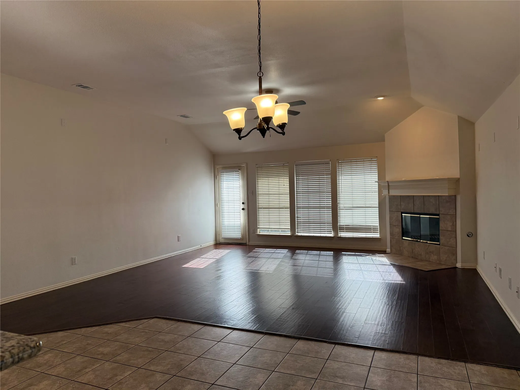 Living area featuring wood-finish flooring, a tiled fireplace with mantel, and multiple windows with blinds