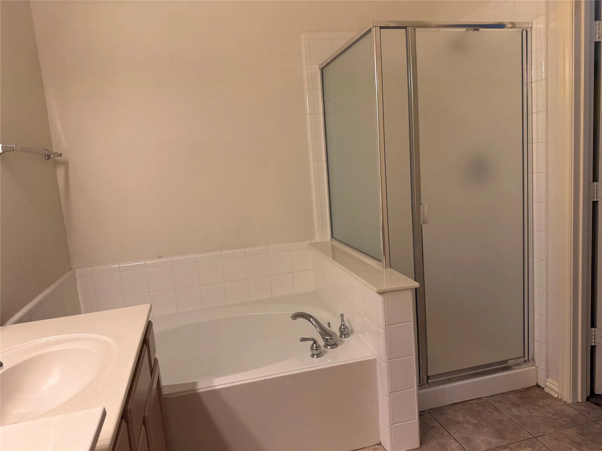 Bathroom featuring a built-in tub with tile surround, a separate shower with a frosted glass enclosure, a vanity with an integrated sink, and tile flooring