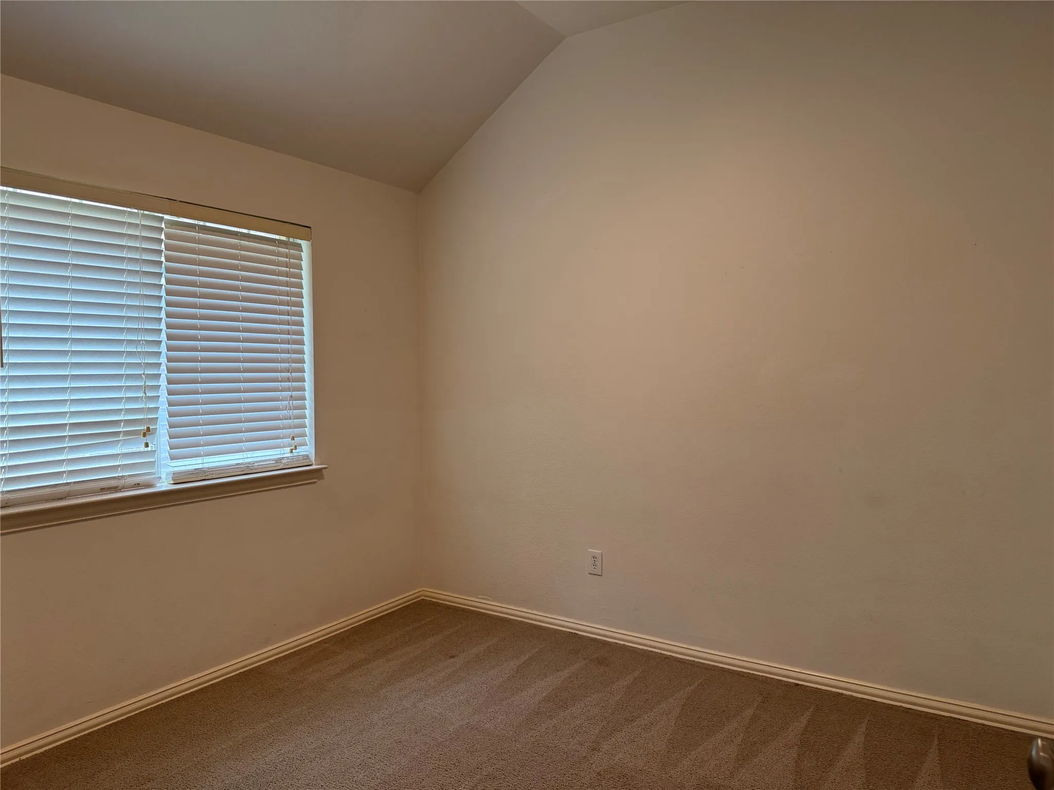 Room featuring sloped ceiling, horizontal window blinds, light-toned walls, contrasting white baseboards, and patterned carpeting
