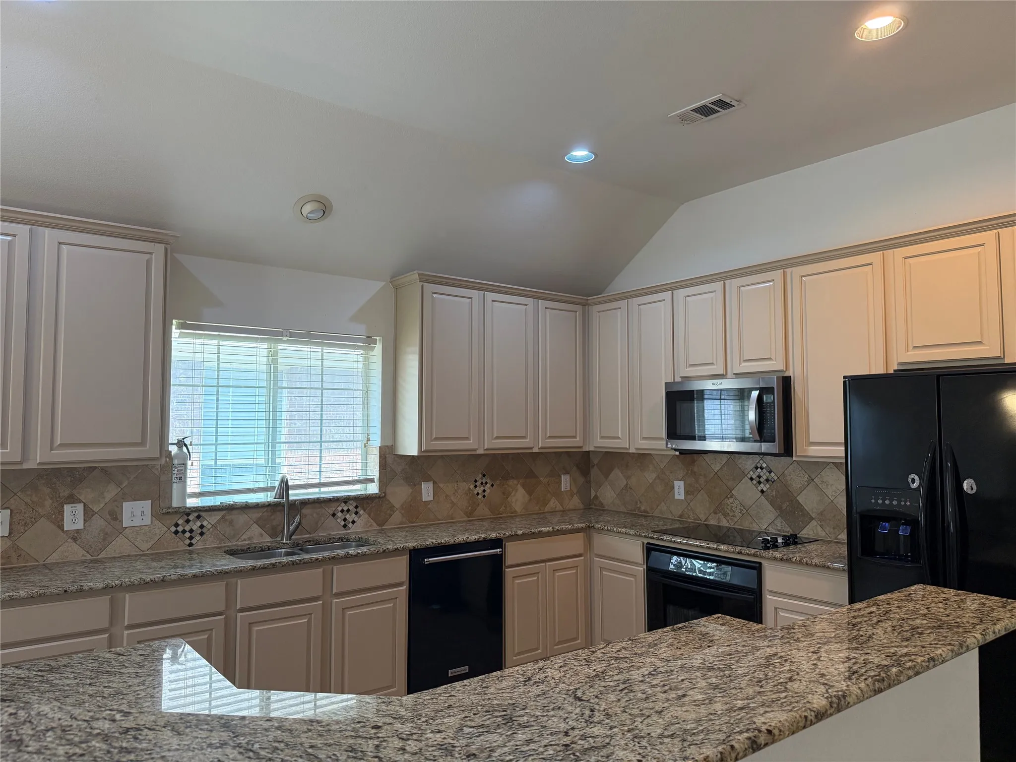 Kitchen featuring light cabinetry, granite countertops, tile backsplash, and a double basin sink