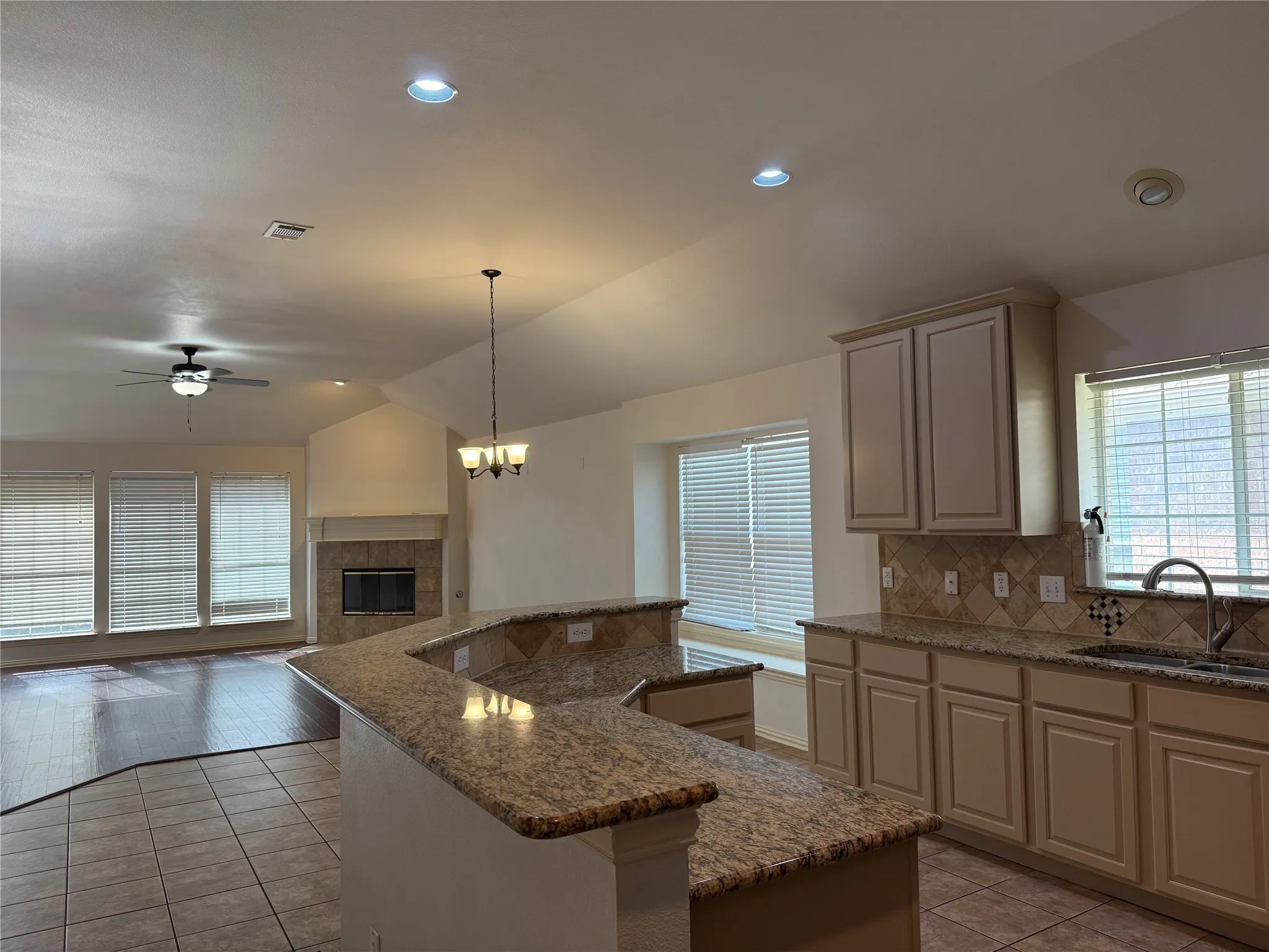 Open concept kitchen and living area featuring granite-look countertops, neutral tile backsplash, recessed lighting, and a built-in fireplace
