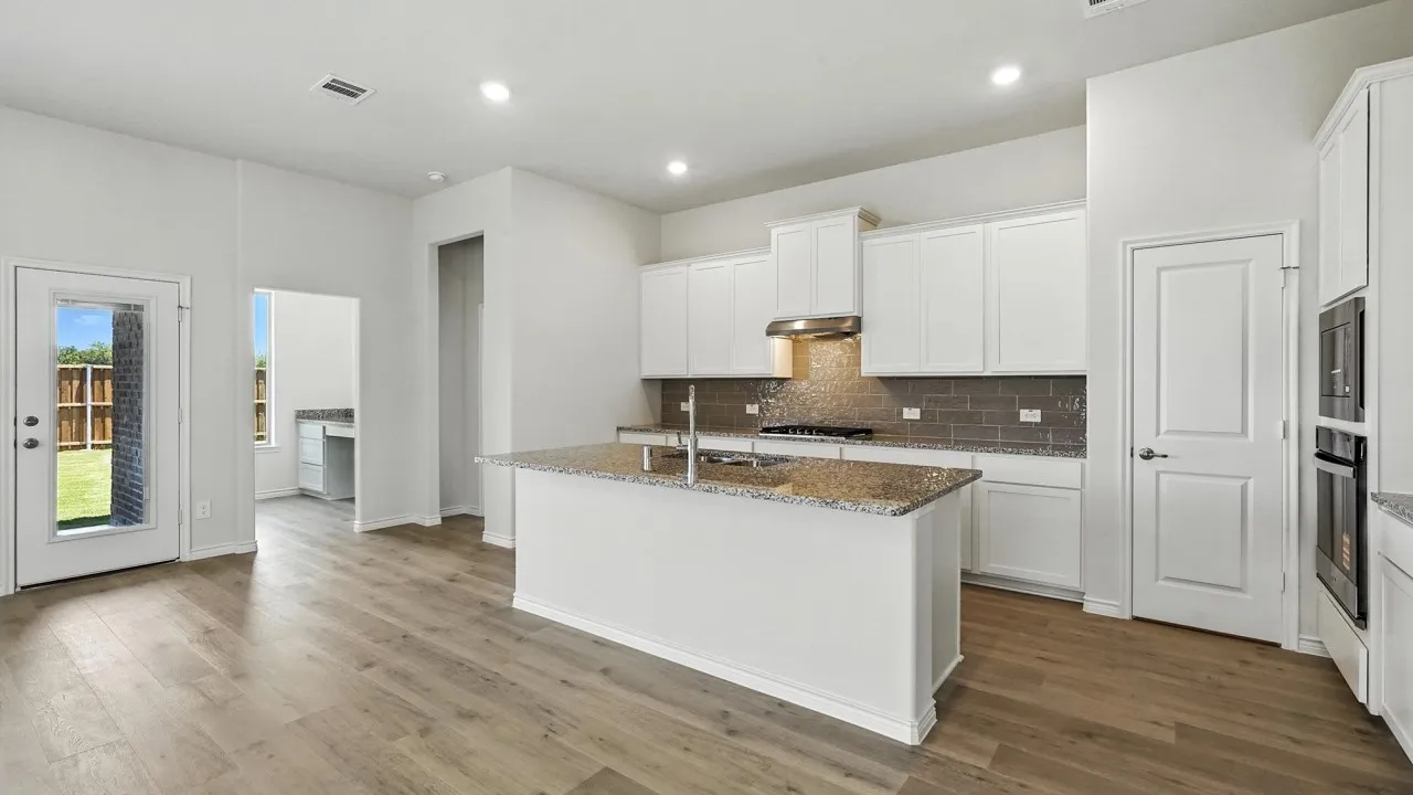 Kitchen featuring a central island with an undermount sink, granite countertops, and white cabinetry