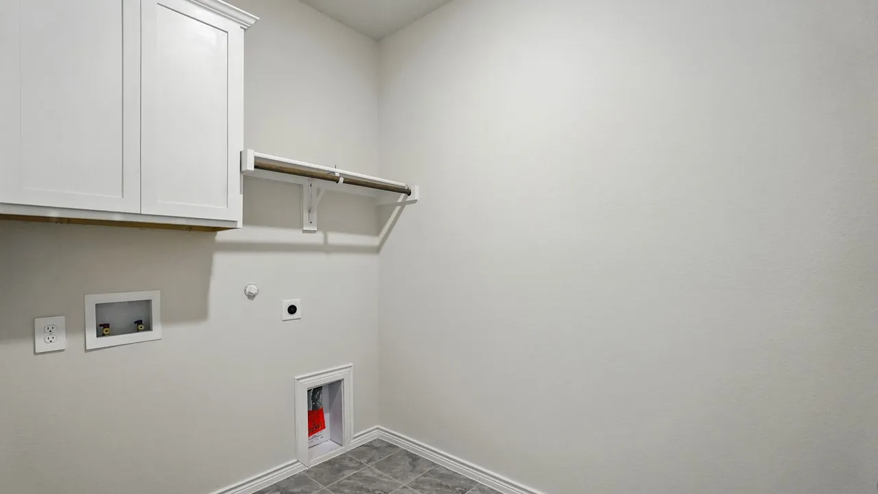 Dedicated utility space featuring white upper cabinetry, a hanging rod, gray tile flooring, and essential appliance hookups