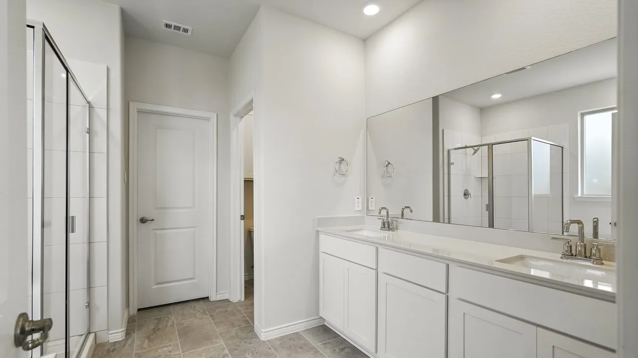 Bathroom featuring a dual vanity with undermount sinks, a spacious mirrored wall, and a tiled walk-in shower with clear glass enclosure