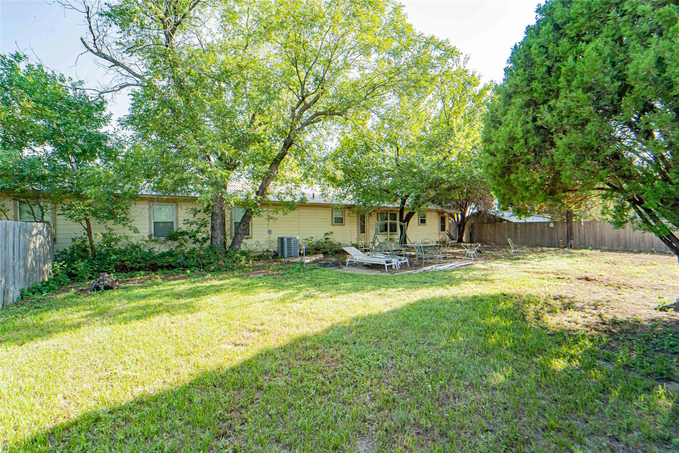 Expansive backyard featuring a large grass area, mature trees, a concrete patio, and privacy fencing