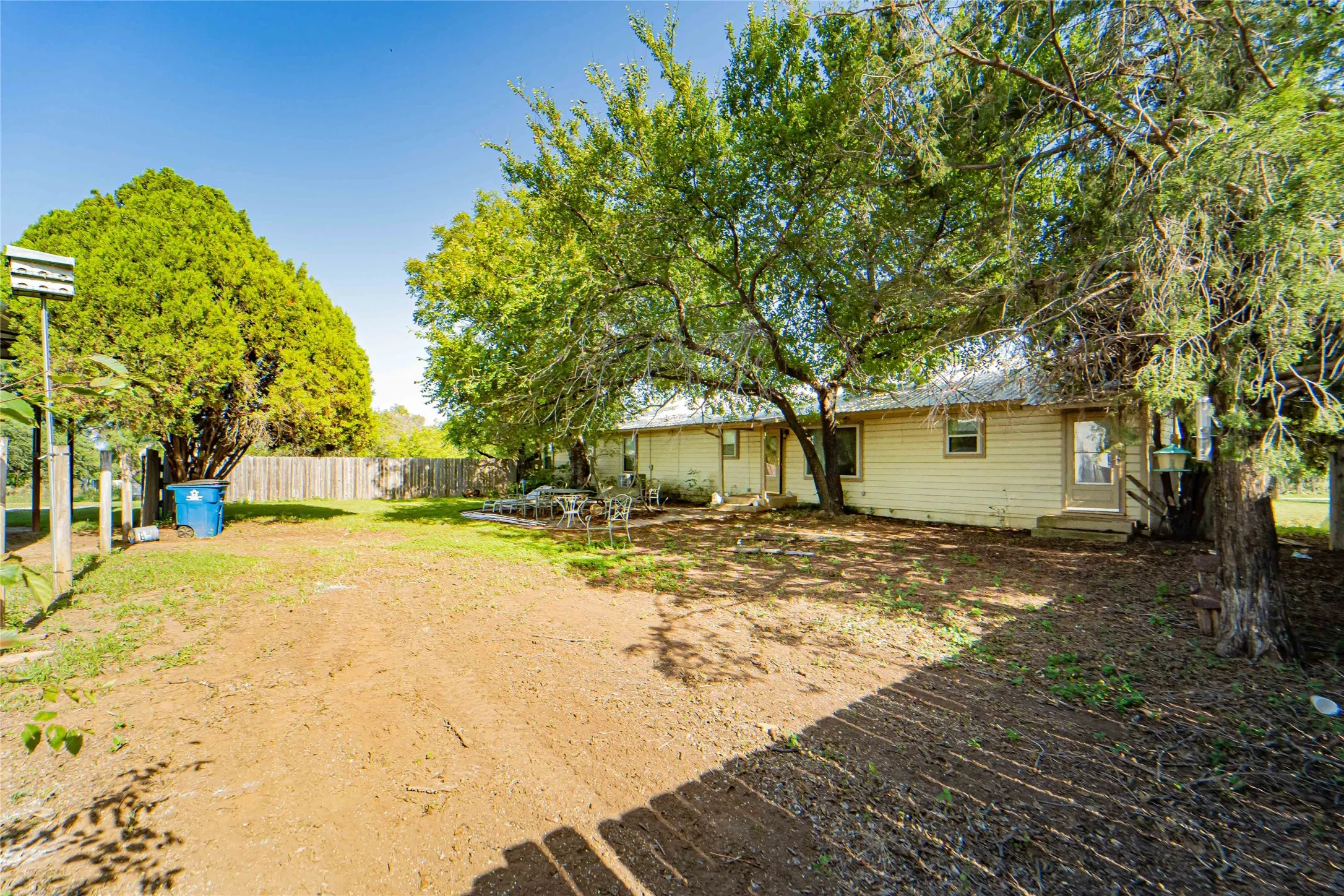 Expansive backyard featuring mature trees, a wood privacy fence, and a neutral-toned exterior with multiple access points