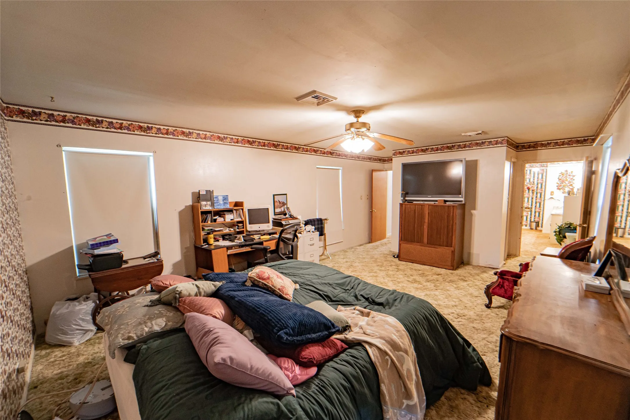 Spacious room featuring broadloom carpet, a ceiling fan with integrated lighting, and a window with a roller shade