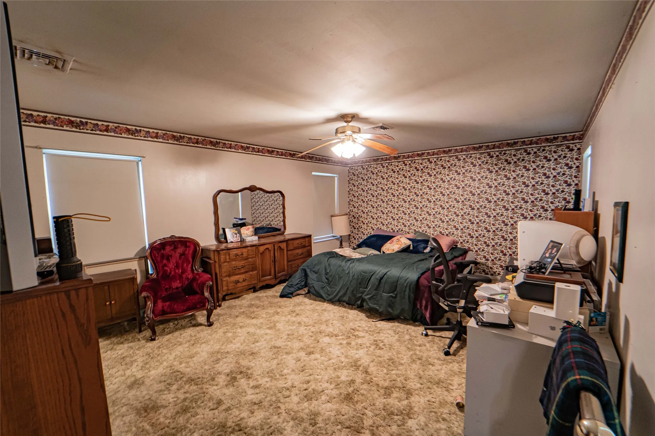 Spacious room featuring broadloom carpet, multiple windows with roller shades, and a ceiling fan with integrated lighting