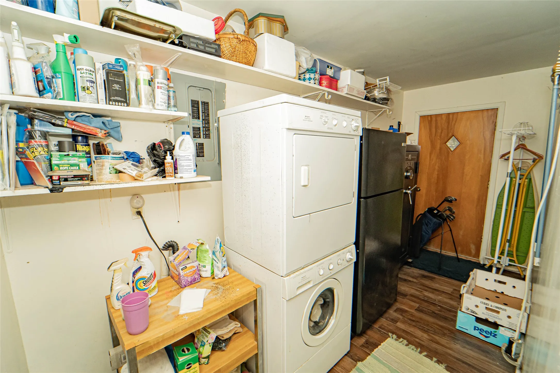 Utility area featuring a stackable washer and dryer, additional refrigeration, wood-finish flooring, and wall-mounted shelving