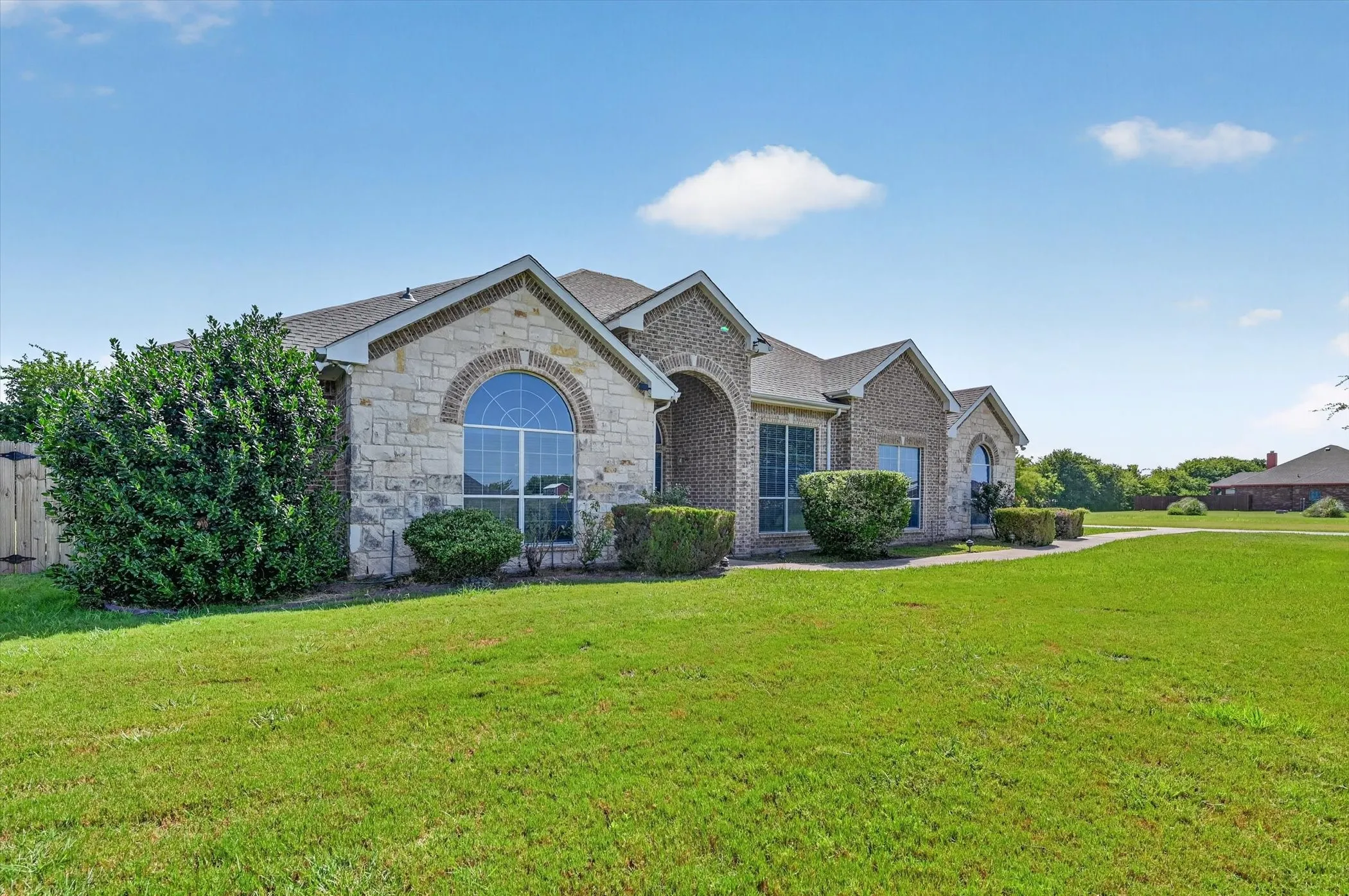 Stone and brick exterior featuring arched windows, established landscaping, and a manicured lawn