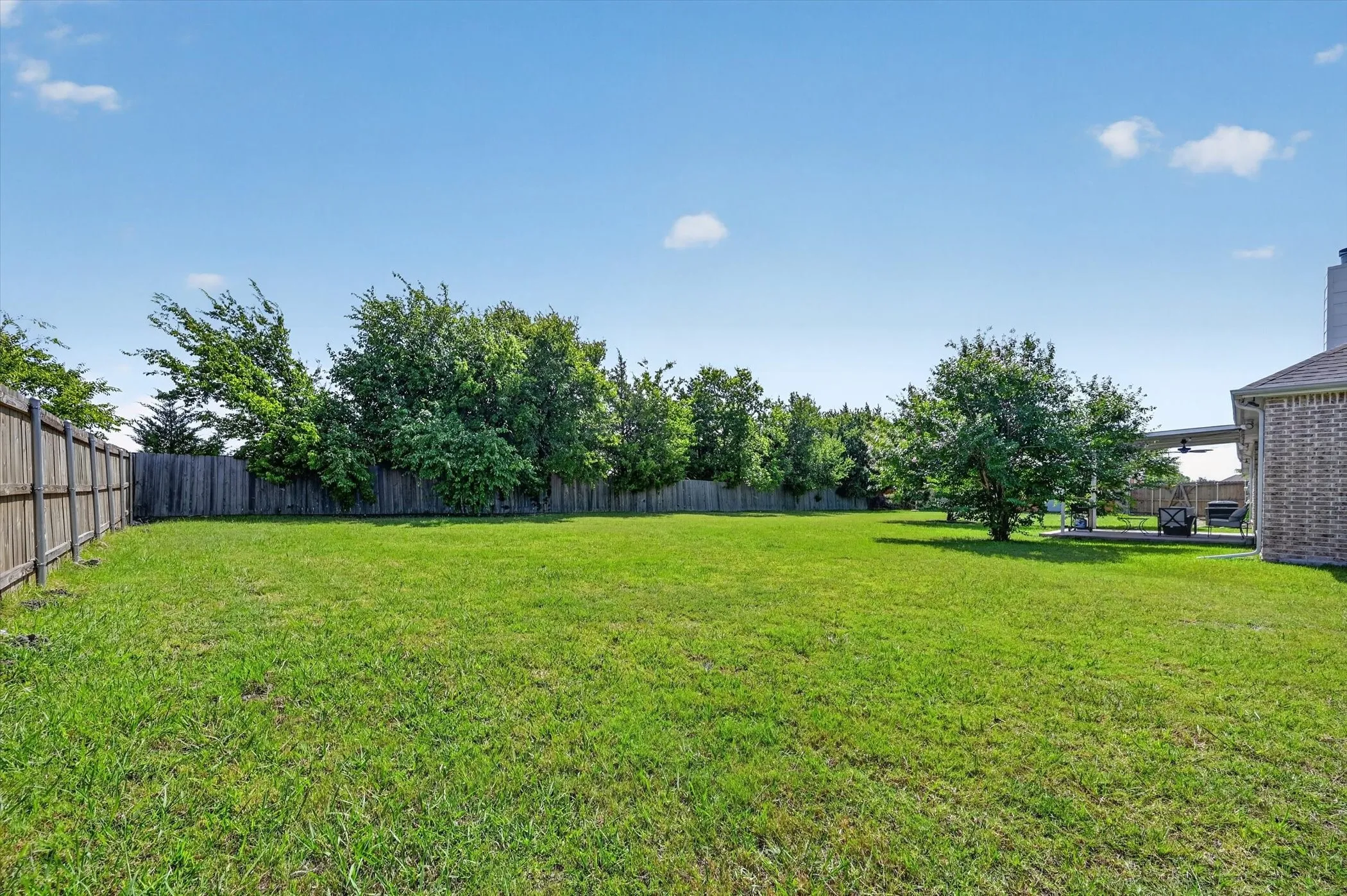 Expansive backyard featuring a manicured lawn, established trees, and perimeter privacy fencing