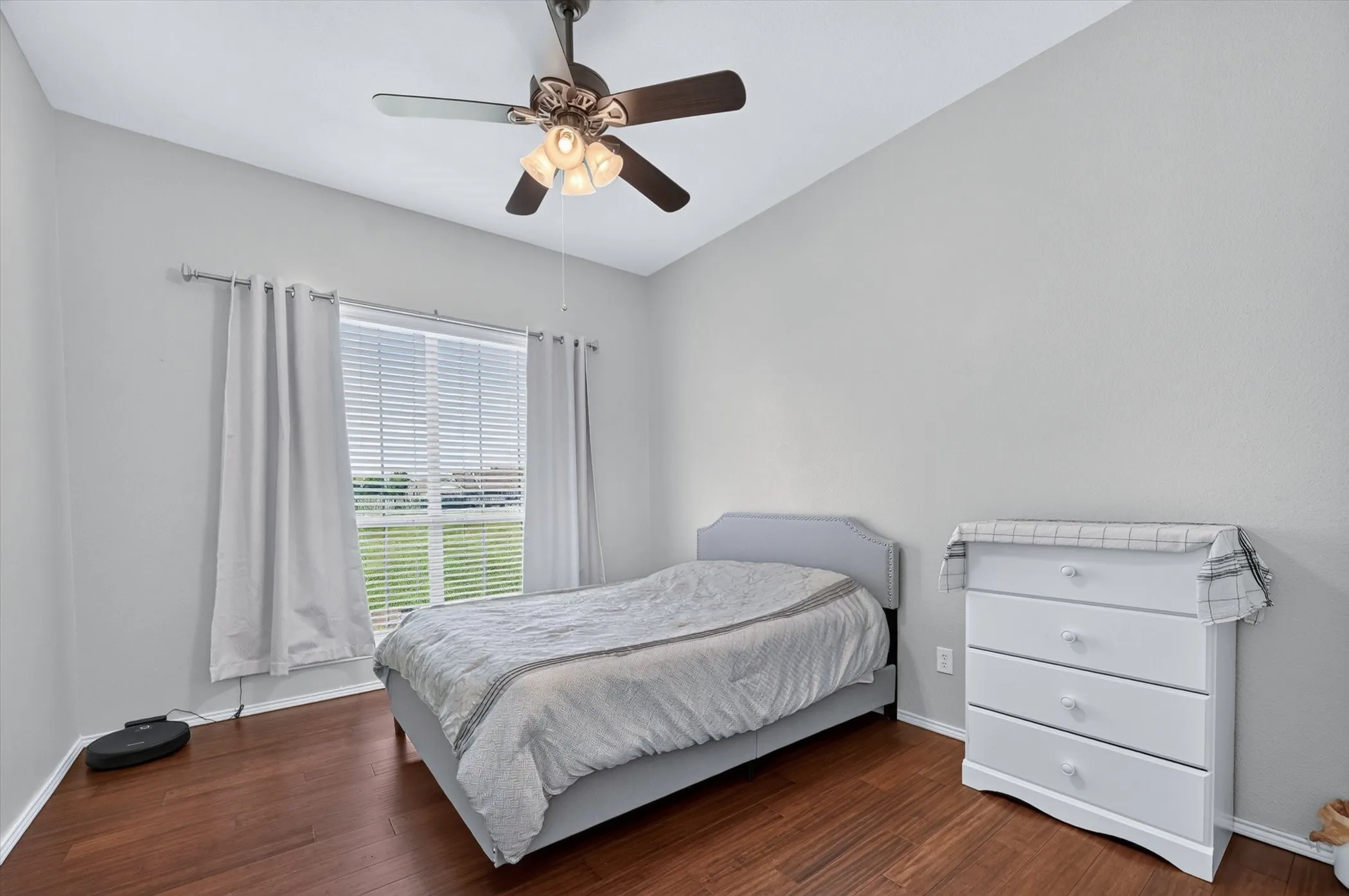 Spacious room featuring vaulted ceilings, a ceiling fan with integrated lighting, wood-finish flooring, and a large window with blinds