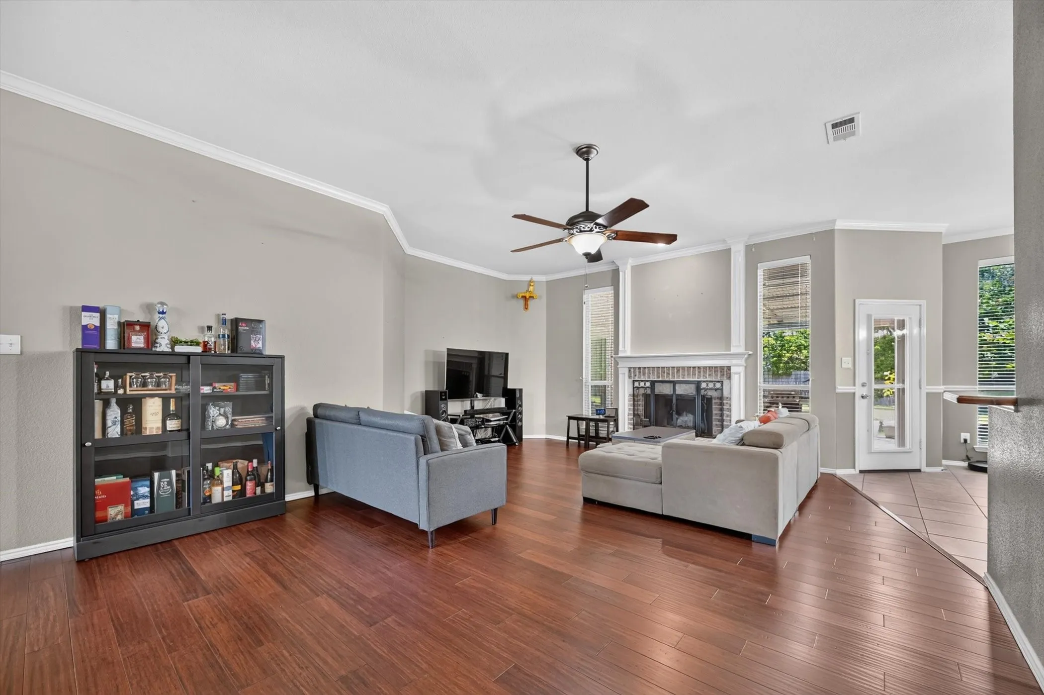 Spacious living area featuring wood-finish flooring, a ceiling fan with light fixture, and crown molding
