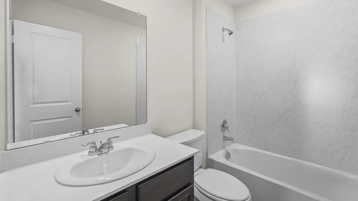 Bathroom featuring a white bathtub with a textured surround, a single vanity with an undermount sink, a chrome faucet, and a large wall-mounted mirror
