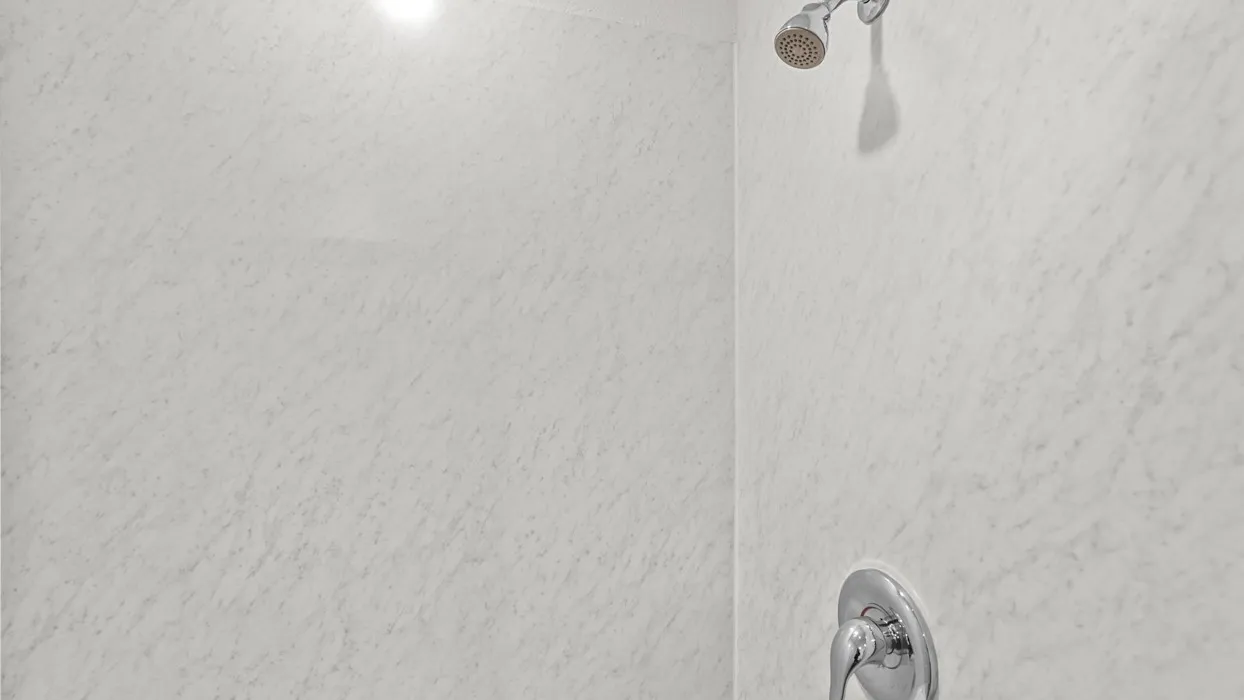 Shower enclosure featuring light-toned, textured wall panels and chrome fixtures including a showerhead and single-handle control