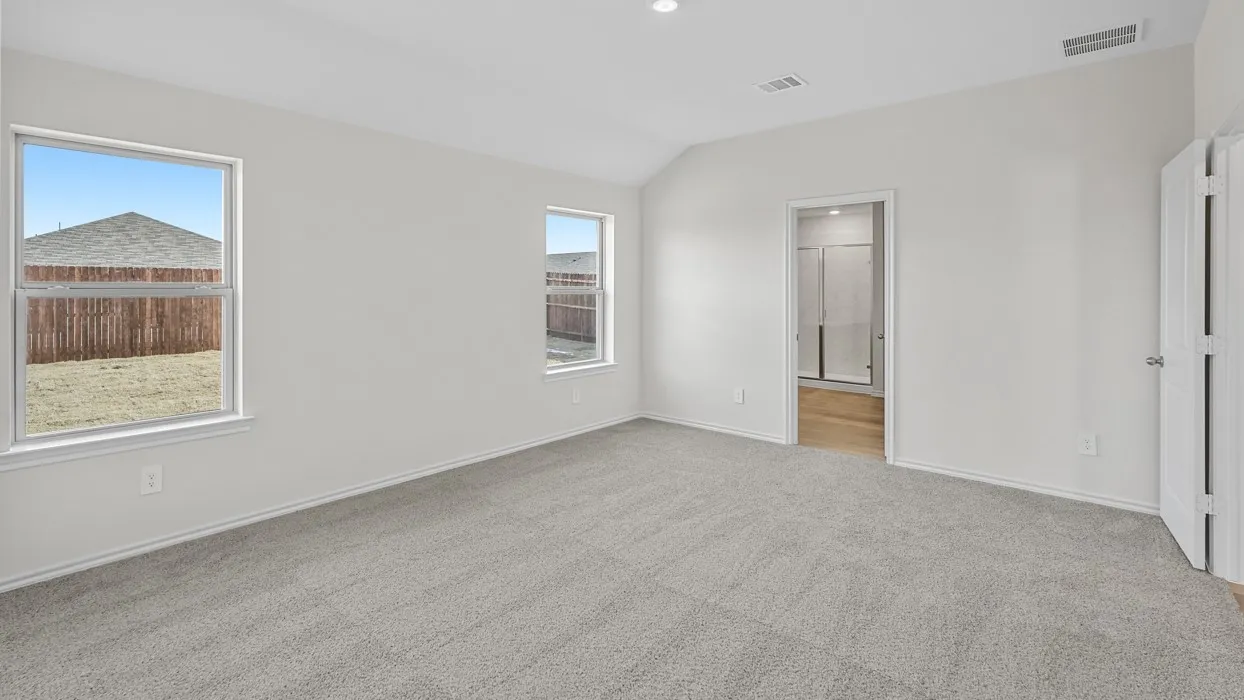 Spacious room featuring vaulted ceilings, light gray carpeting, two windows, and a doorway leading to a bathroom with wood-finish flooring