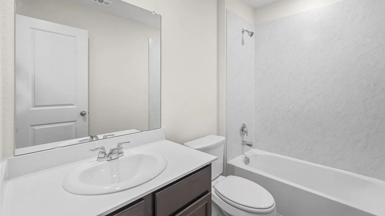 Bathroom featuring a white bathtub with a shower, a dark wood-finish vanity with a light countertop, an undermount sink, and a large wall-mounted mirror