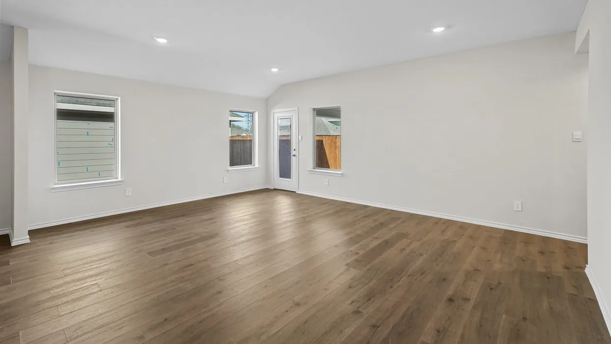 Spacious room featuring wood-finish flooring, white walls, multiple windows, a rear exterior door, and recessed lighting