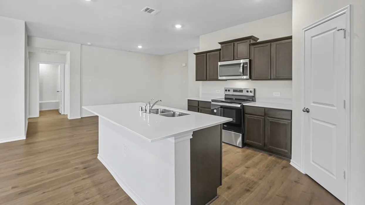 Contemporary kitchen featuring a spacious island with an undermount double sink, dark wood-finish cabinetry, stainless steel appliances, and wood-finish flooring
