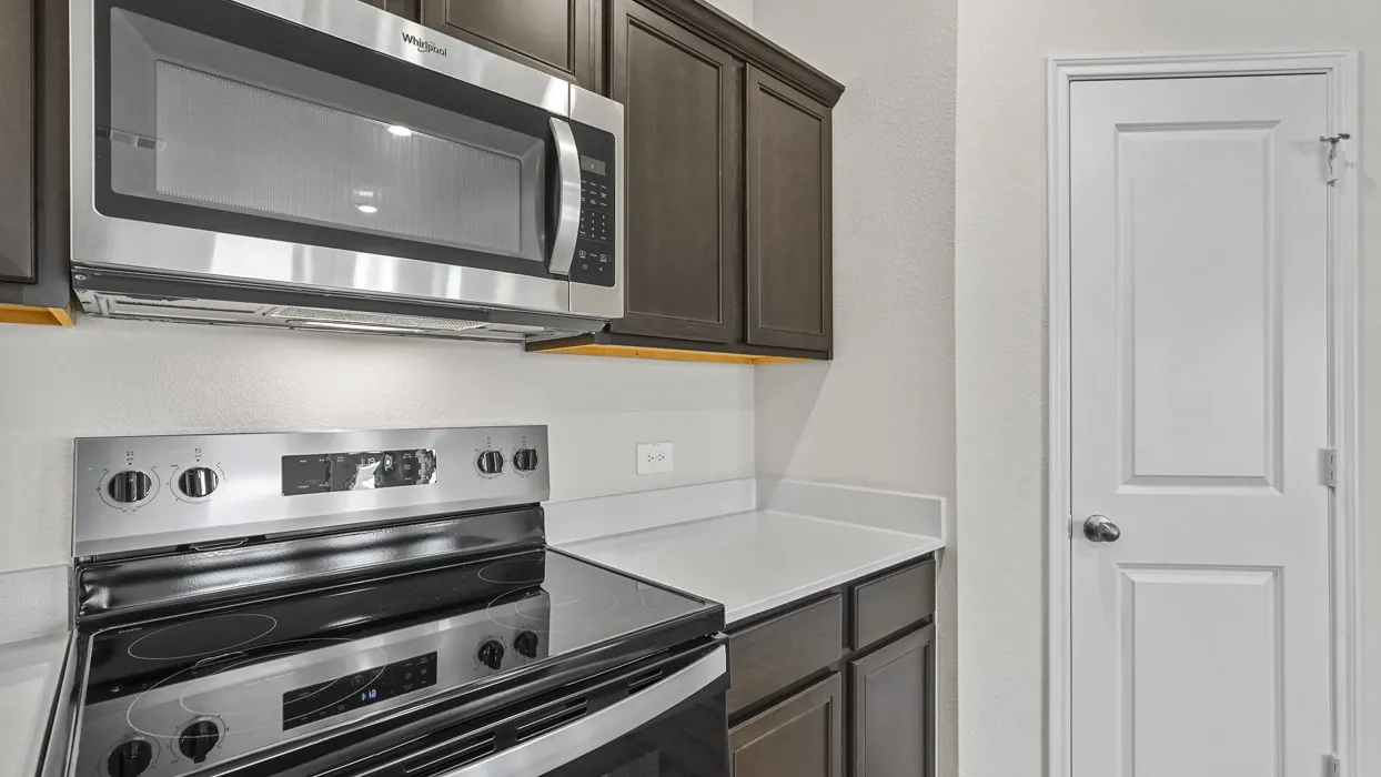 Kitchen featuring stainless steel appliances, dark wood cabinetry, white countertops, and under-cabinet lighting