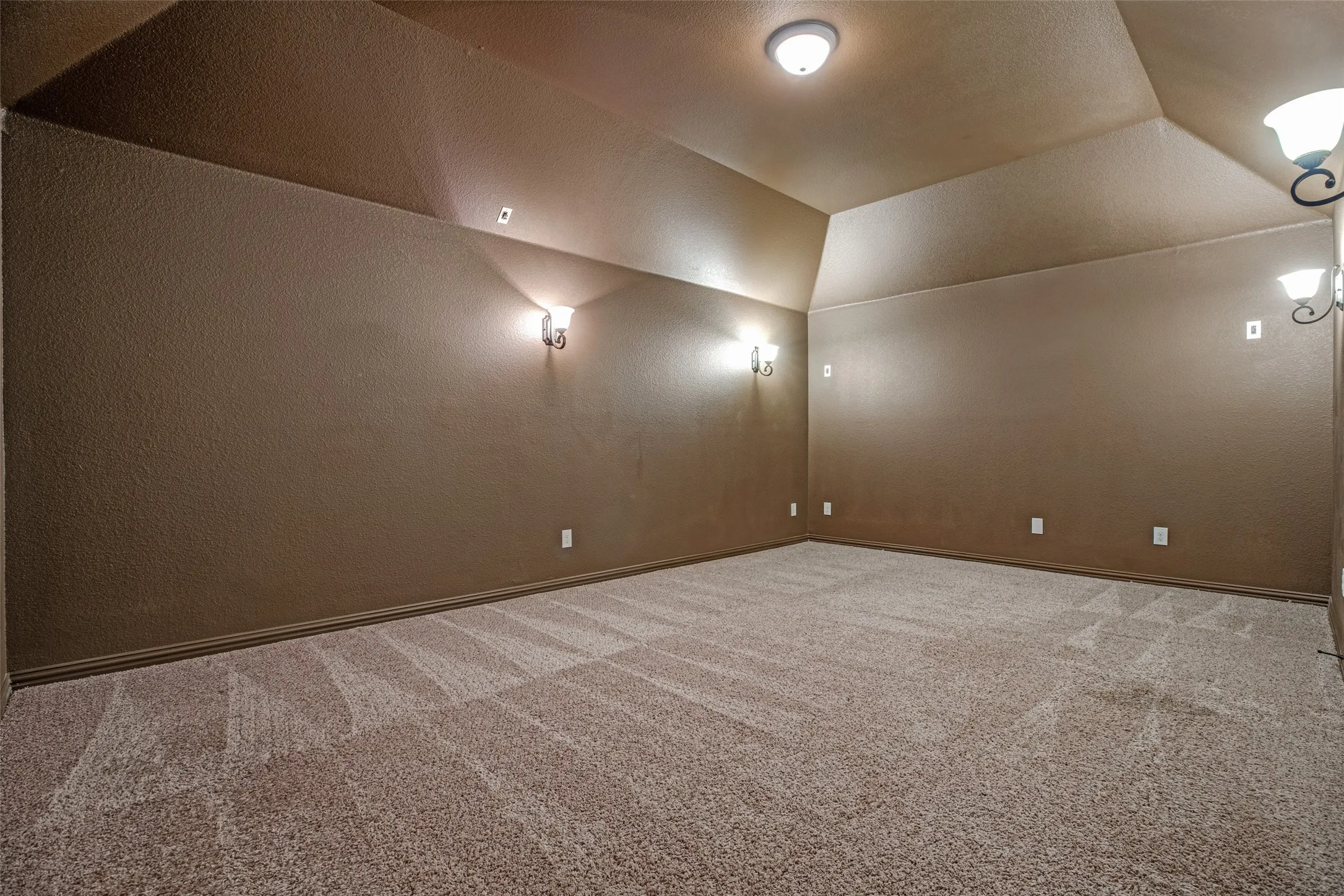Carpeted room featuring sconce lighting, a vaulted ceiling, textured walls, and base molding