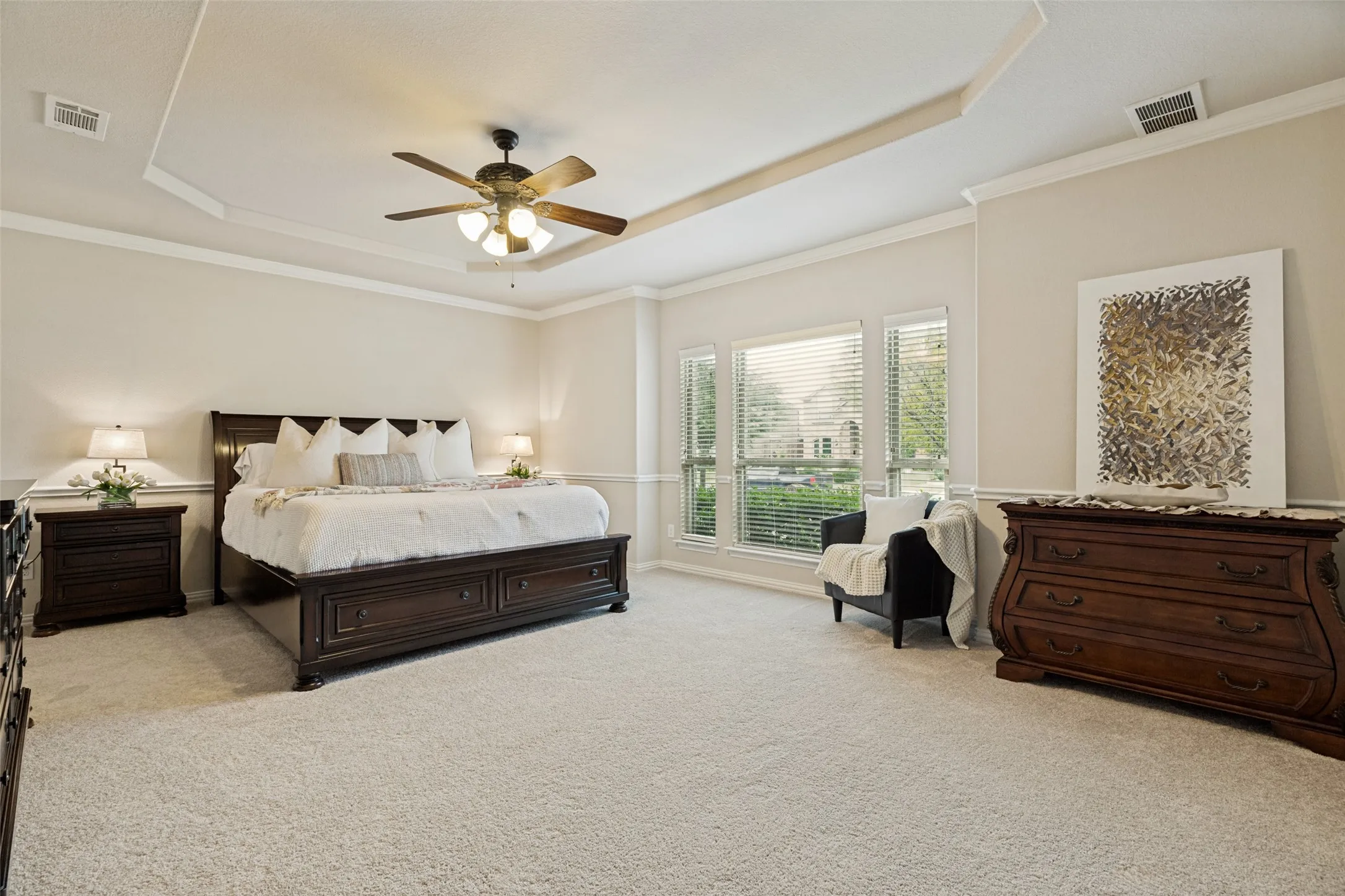 Carpeted interior space featuring a tray ceiling with crown molding, multiple windows, and a ceiling fan