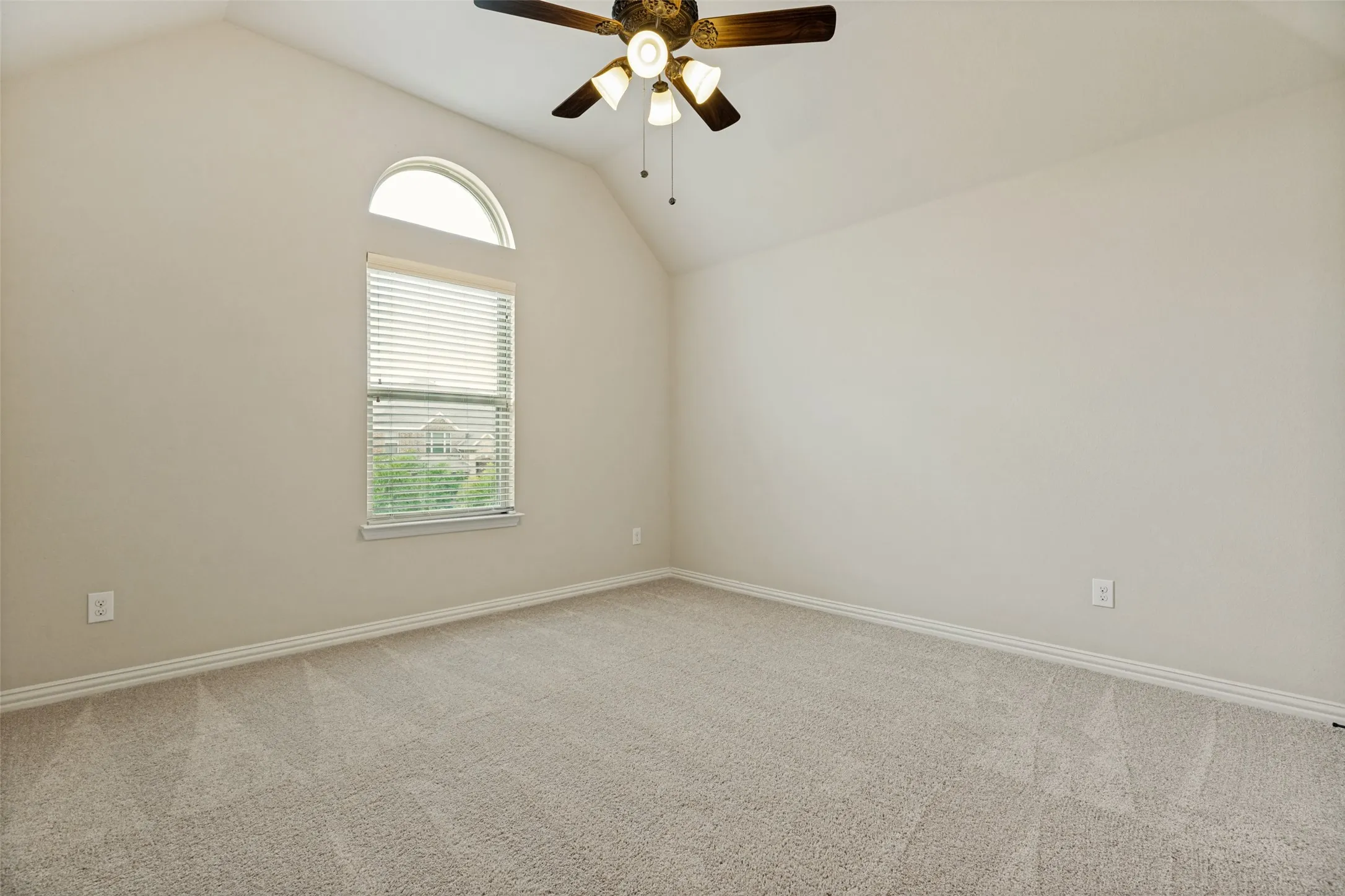 Carpeted room featuring a vaulted ceiling, a window with horizontal blinds, and an arched transom window
