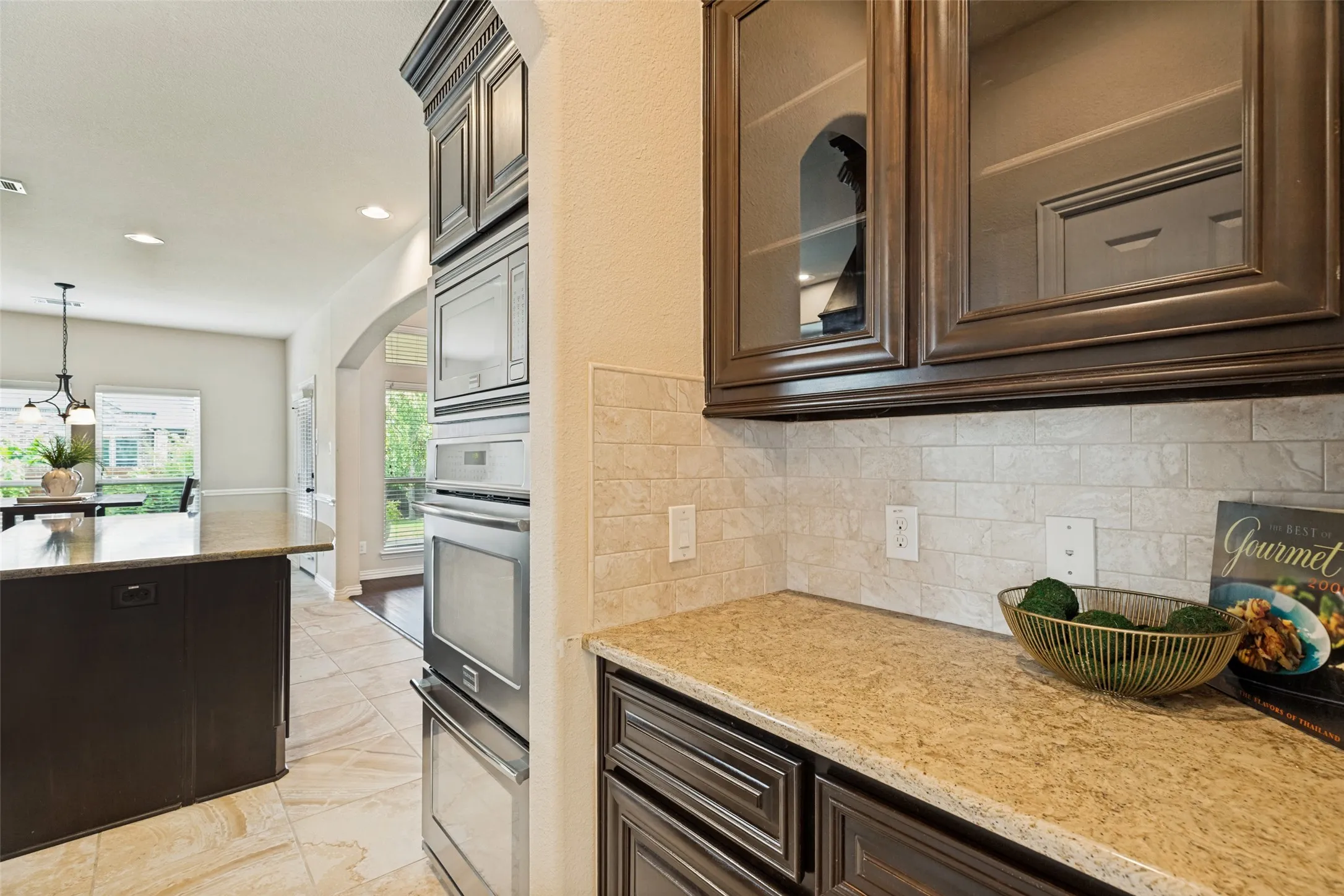 Kitchen featuring built-in stainless steel appliances, dark wood cabinetry, light-toned backsplash, and a stone-finish countertop